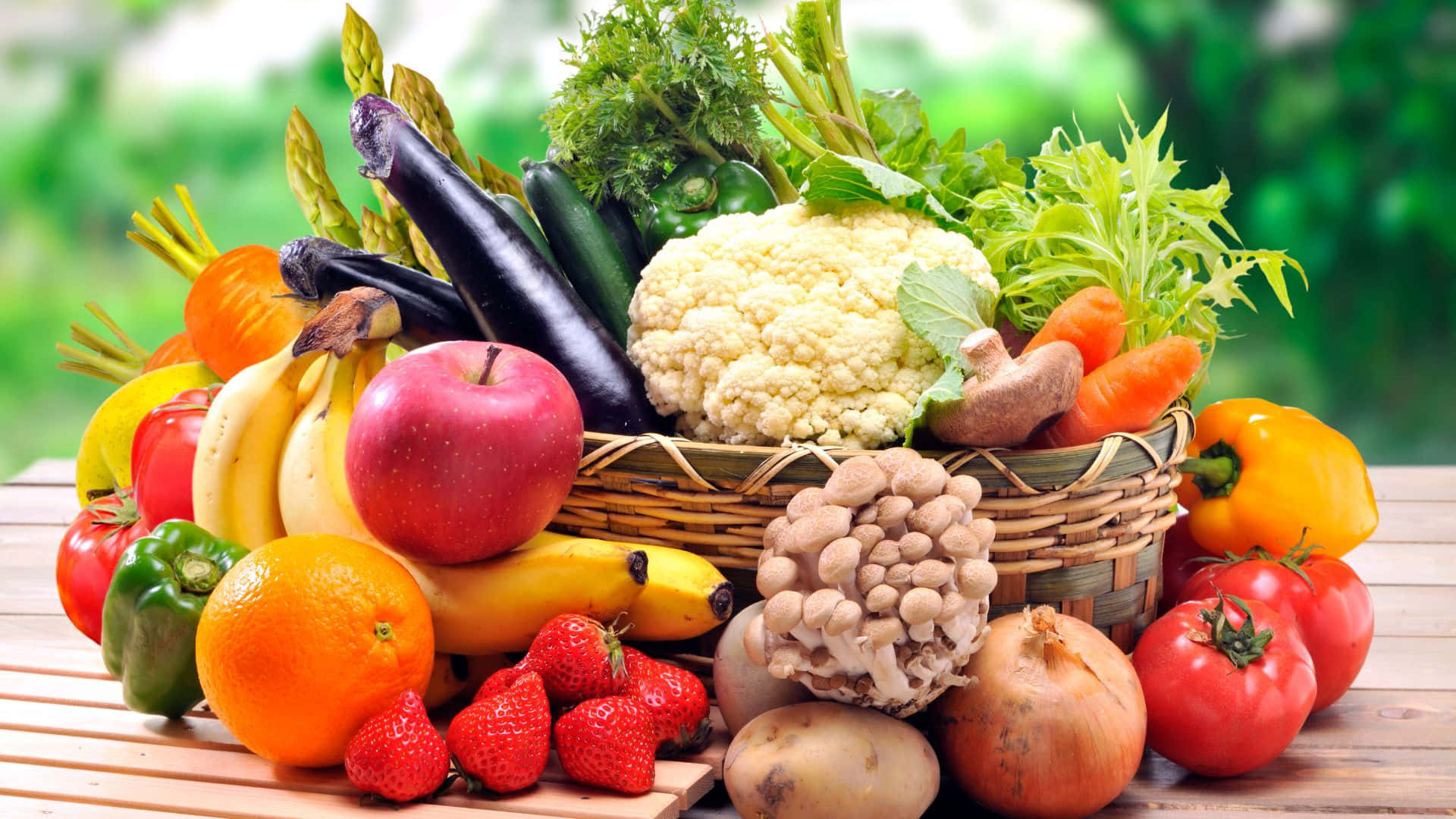 Fruits And Vegetables 桌布 壁紙 — 一個充滿活力的籃子，裝滿新鮮水果和蔬菜，擺放在木桌上，背景是模糊的綠色。