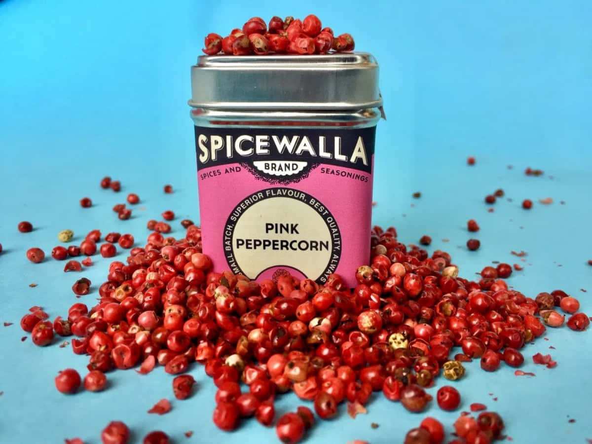 Pink Peppercorn 桌布 壁紙 — 一個充滿活力的粉紅胡椒罐，裝滿鮮紅色的漿果，襯著純藍色背景。