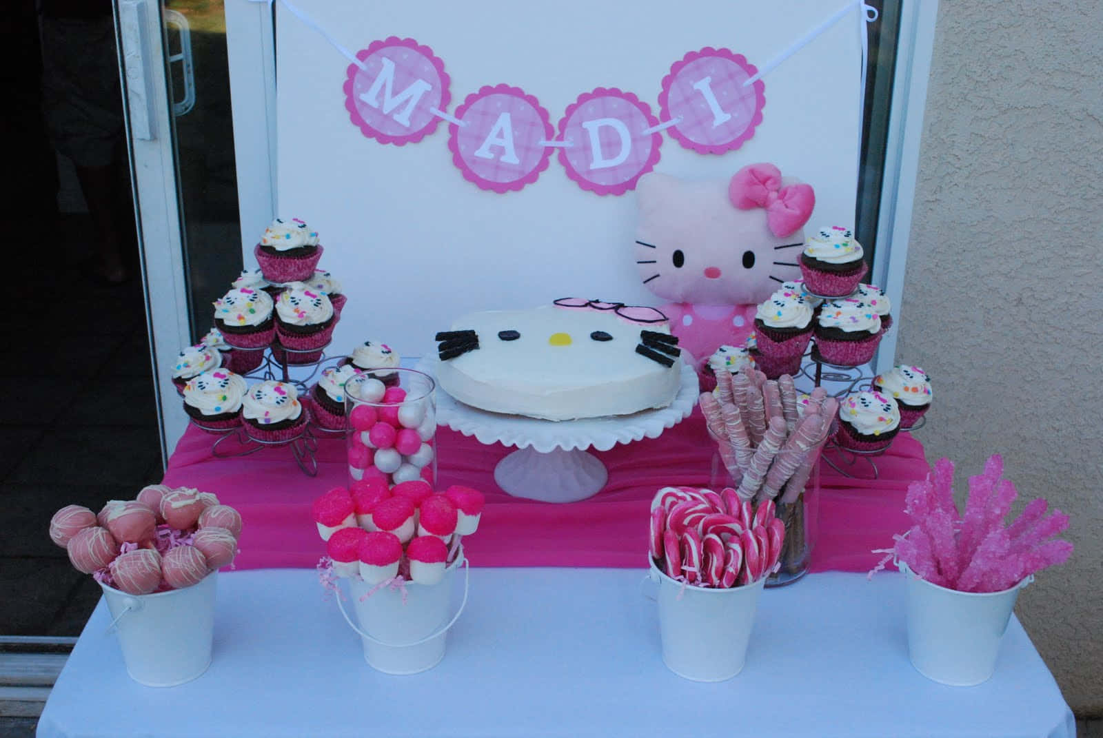 Hello Kitty Birthday 桌布 壁紙 — 一個充滿活力的粉紅色Hello Kitty生日甜品桌，在名字橫幅下擺放著杯子蛋糕、蛋糕和糖果。