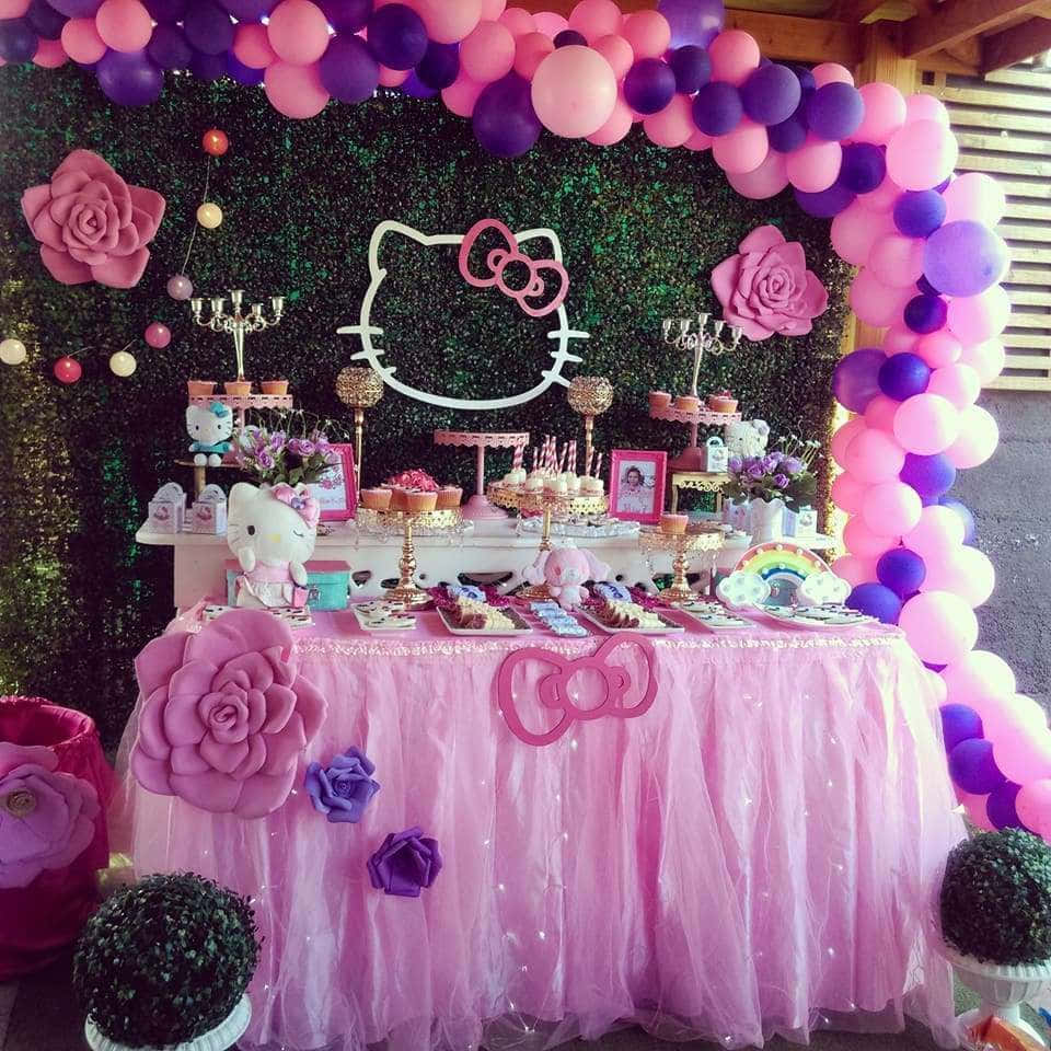 Hello Kitty Party 桌布 壁紙 — 一個充滿活力的粉紅色和紫色Hello Kitty生日派對佈置，配有氣球拱門、巨型紙玫瑰和裝飾好的甜品桌。