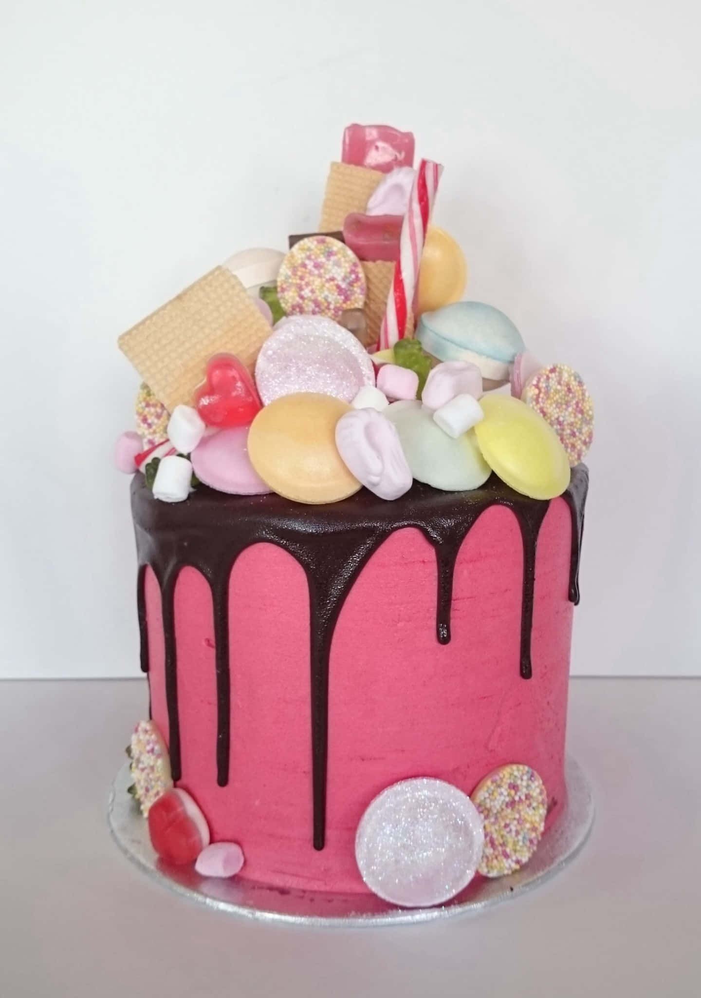 Cake Fondant 桌布 壁紙 — 一個充滿活力的粉紅色蛋糕，上面有朱古力滴落和色彩繽紛的糖果和餅乾堆疊。