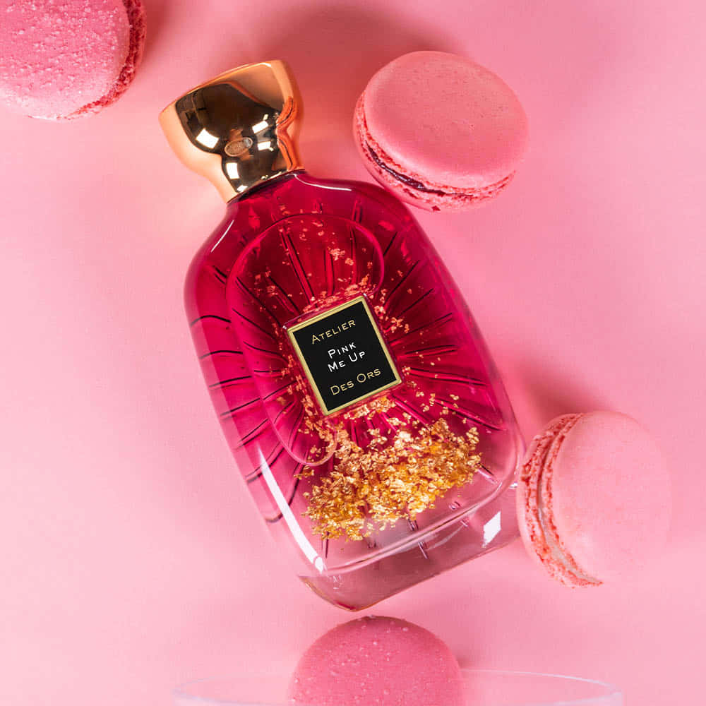 Floral Fragrance 桌布 壁紙 — 一個充滿活力的粉紅色香水瓶，帶有金色閃粉和金色瓶蓋，放置在柔和的粉紅色背景上，周圍環繞著粉紅色馬卡龍。
