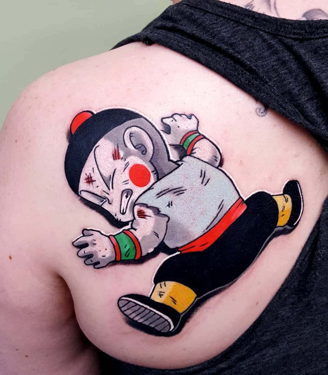 Chiaotzu 桌布 壁紙 — 一個充滿活力的紋身，描繪一個卡通風格的武術家，臉頰紅潤，戴著黑色帽子，位於一個人的肩膀上。