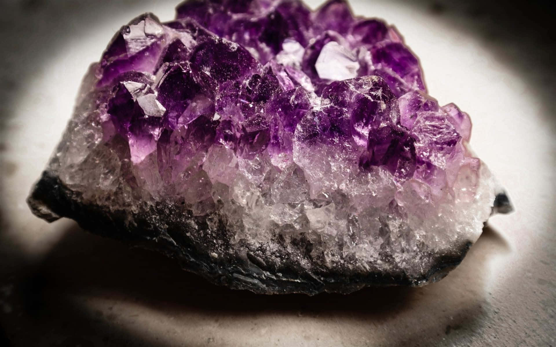 Amethyst 桌布 壁紙 — 一個充滿活力的紫色紫水晶晶體簇的特寫，具有清晰的切面和深色底座，由柔和的定向光照明。