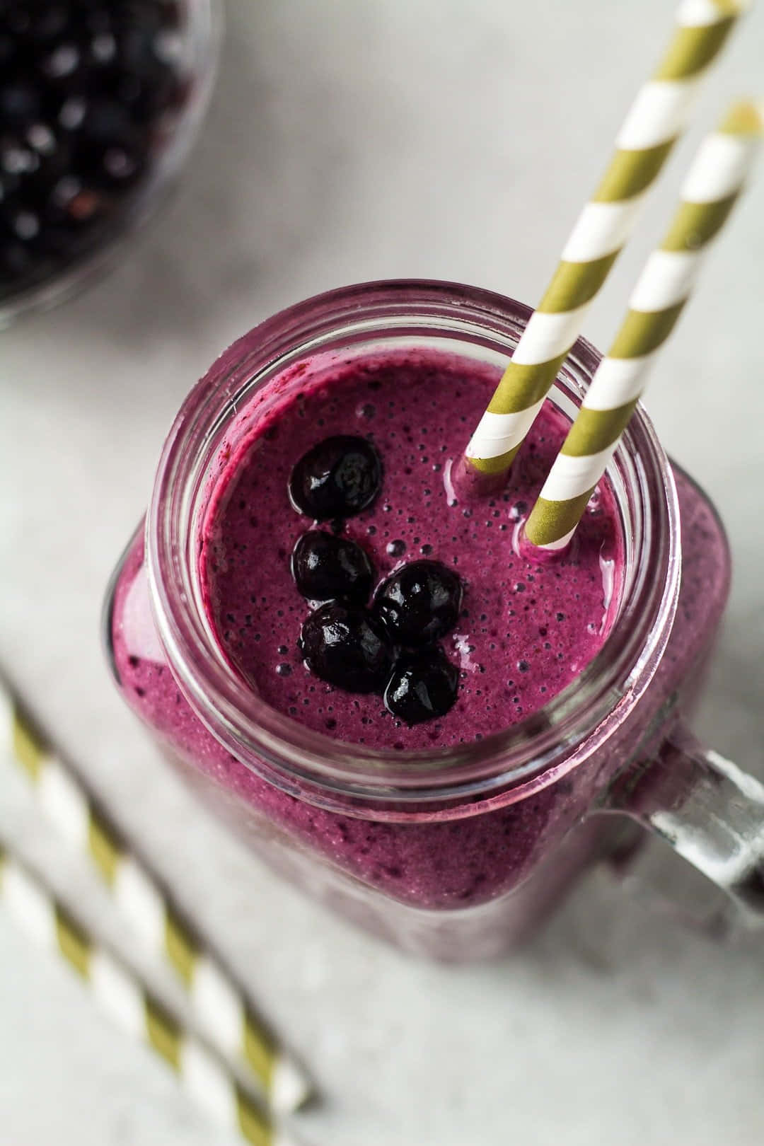 Blueberry Smoothie 桌布 壁紙 — 一個充滿活力的紫色藍莓冰沙放在玻璃罐中，上面放上新鮮莓果和條紋吸管。
