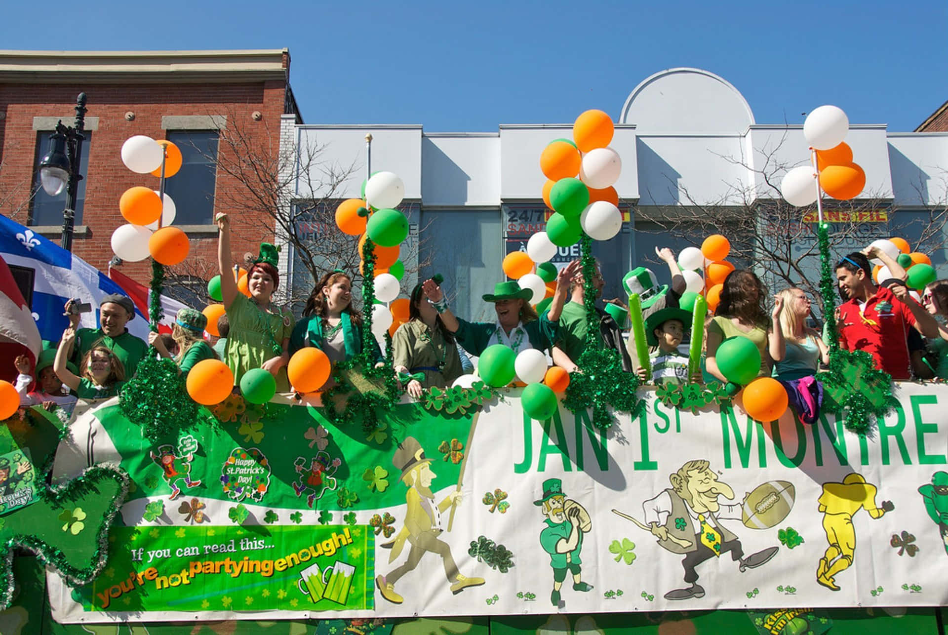 St Patrick's Day 桌布 壁紙 — 一個充滿活力的聖帕特里克節巡遊花車，人們穿著綠色服裝，在晴朗的藍天下揮舞氣球和歡呼。