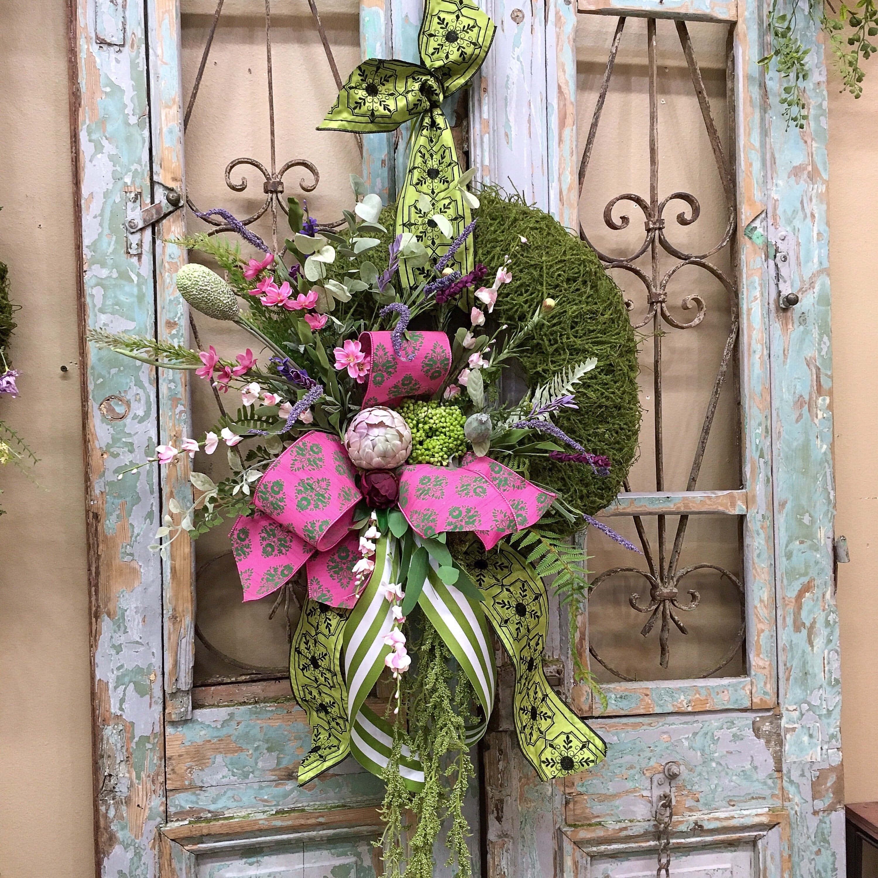 Spring Wreaths 桌布 壁紙 — 一個充滿活力的花環，帶有粉紅色和綠色的絲帶，掛在一個帶有華麗鐵藝的風化青綠色門上。