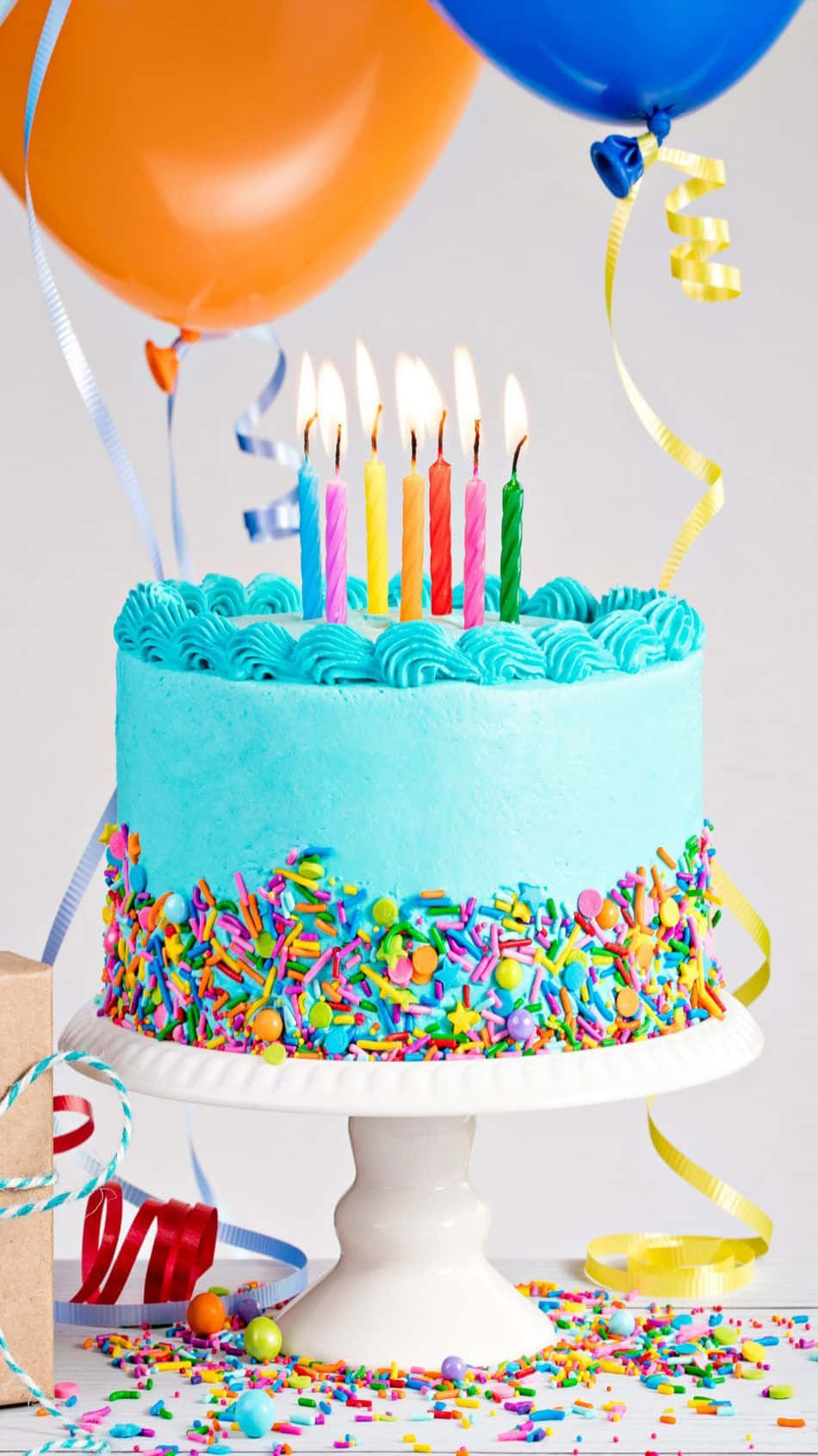  壁紙 — 一個充滿活力的藍色生日蛋糕，上面有燃燒的蠟燭和彩色糖粒，周圍環繞著氣球和彩帶。