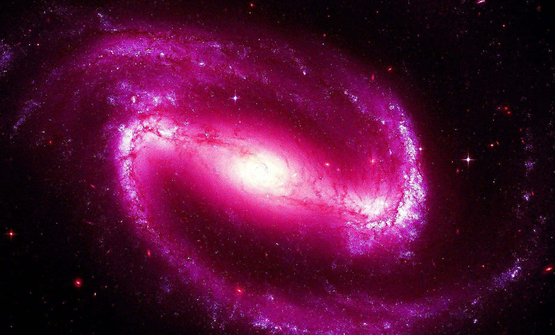 Pink Galaxy 桌布 壁紙 — 一個充滿活力的螺旋星系在佈滿星點的宇宙虛空中散發出洋紅色和粉紅色的光芒。