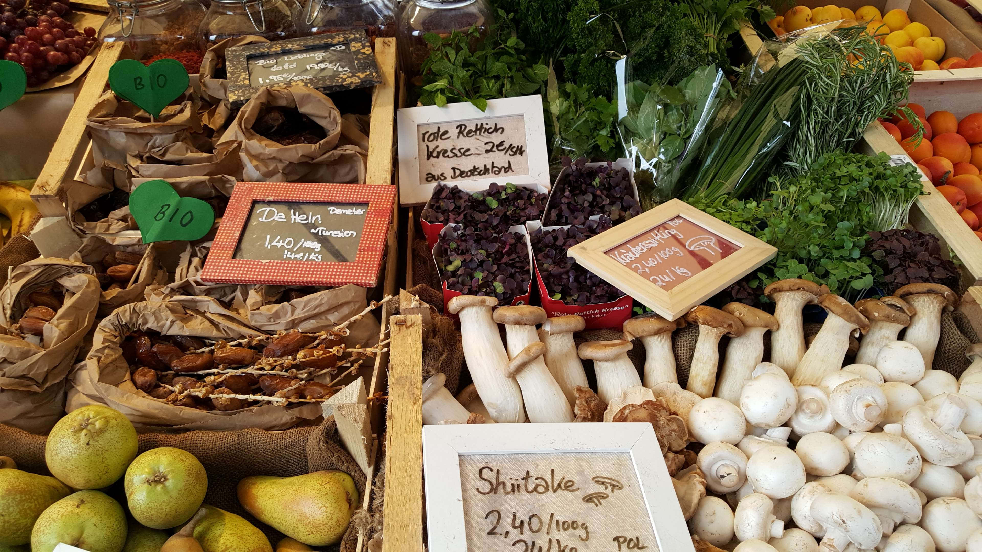 Farmers Market 桌布 壁紙 — 一個充滿活力的農夫市場攤位，擺滿新鮮有機農產品，包括蘑菇、梨、香草和漿果，放在木箱中，附有手寫價格標籤。