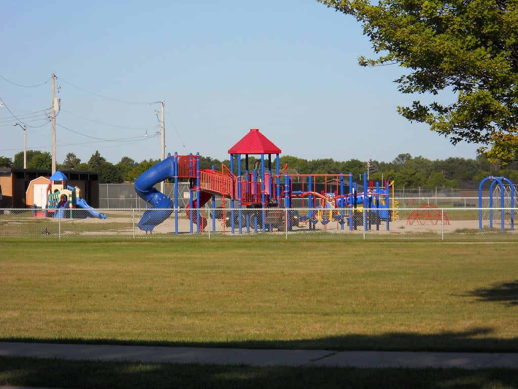 Playground 桌布 壁紙 — 一個充滿活力的遊樂場，設有藍色滑梯和紅色屋頂，矗立在晴朗藍天下的草地上。