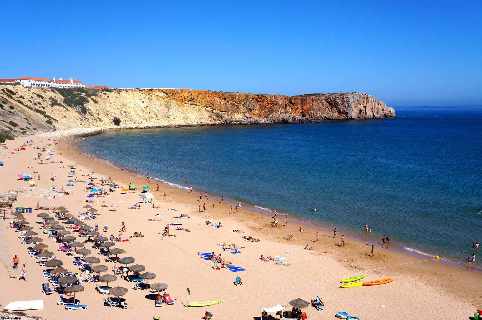 Portuguese Beach 桌布 壁紙 — 一個充滿活力的陽光明媚海灘場景，有碧綠的海水、懸崖和人們在遮陽傘下放鬆。