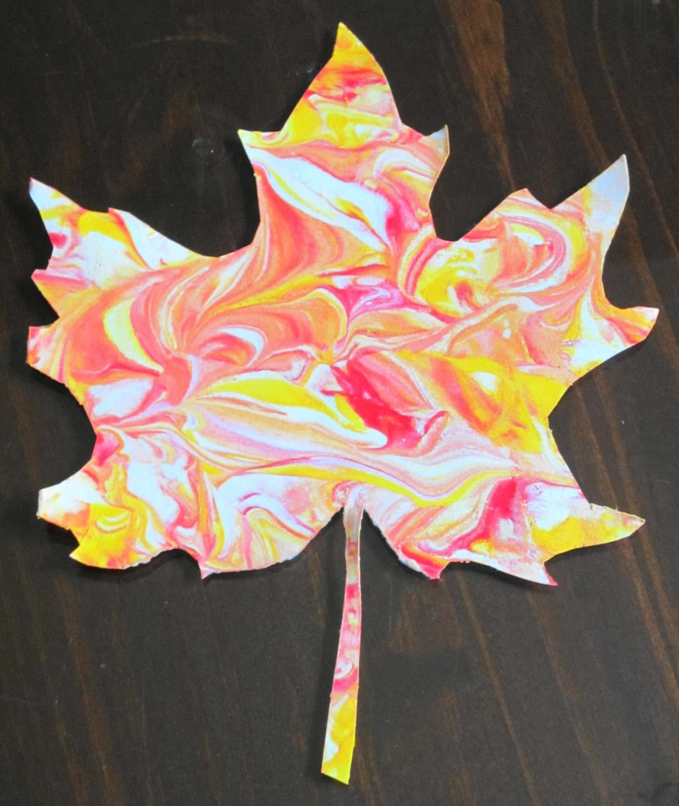 Fall Crafts 桌布 壁紙 — 一個充滿活力的雲石紋楓葉剪影，帶有旋轉的粉紅、黃色和白色圖案，放置在深色木質表面上。