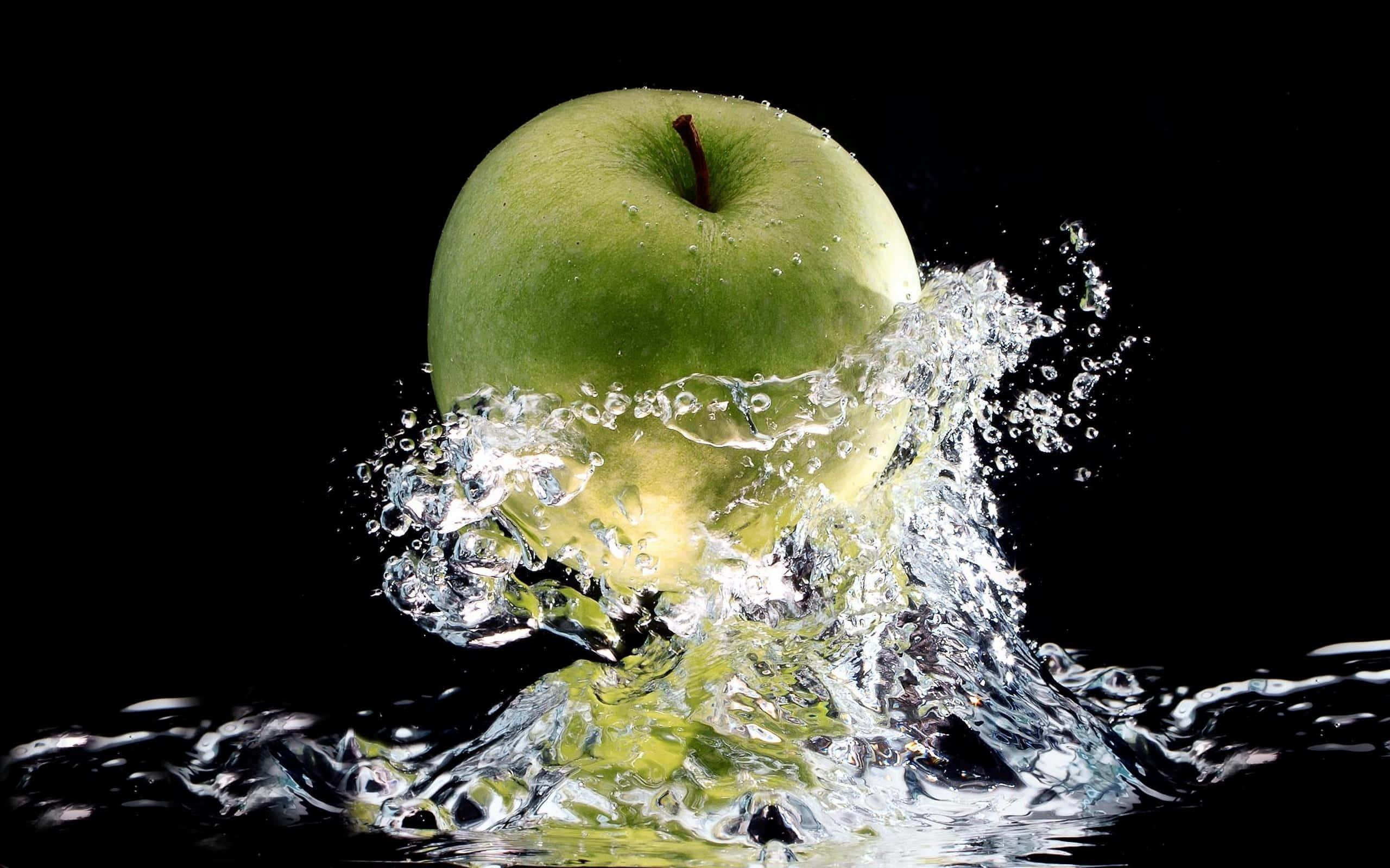 Refreshing 桌布 壁紙 — 一個充滿活力的青蘋果衝破清澈的水面，在純黑背景上形成動態的水花和水滴。