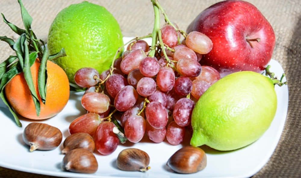 Winter Fruits 桌布 壁紙 — 一個充滿活力的靜物畫，包括葡萄、蘋果、橙子和栗子等新鮮水果，擺放在白色盤子上。