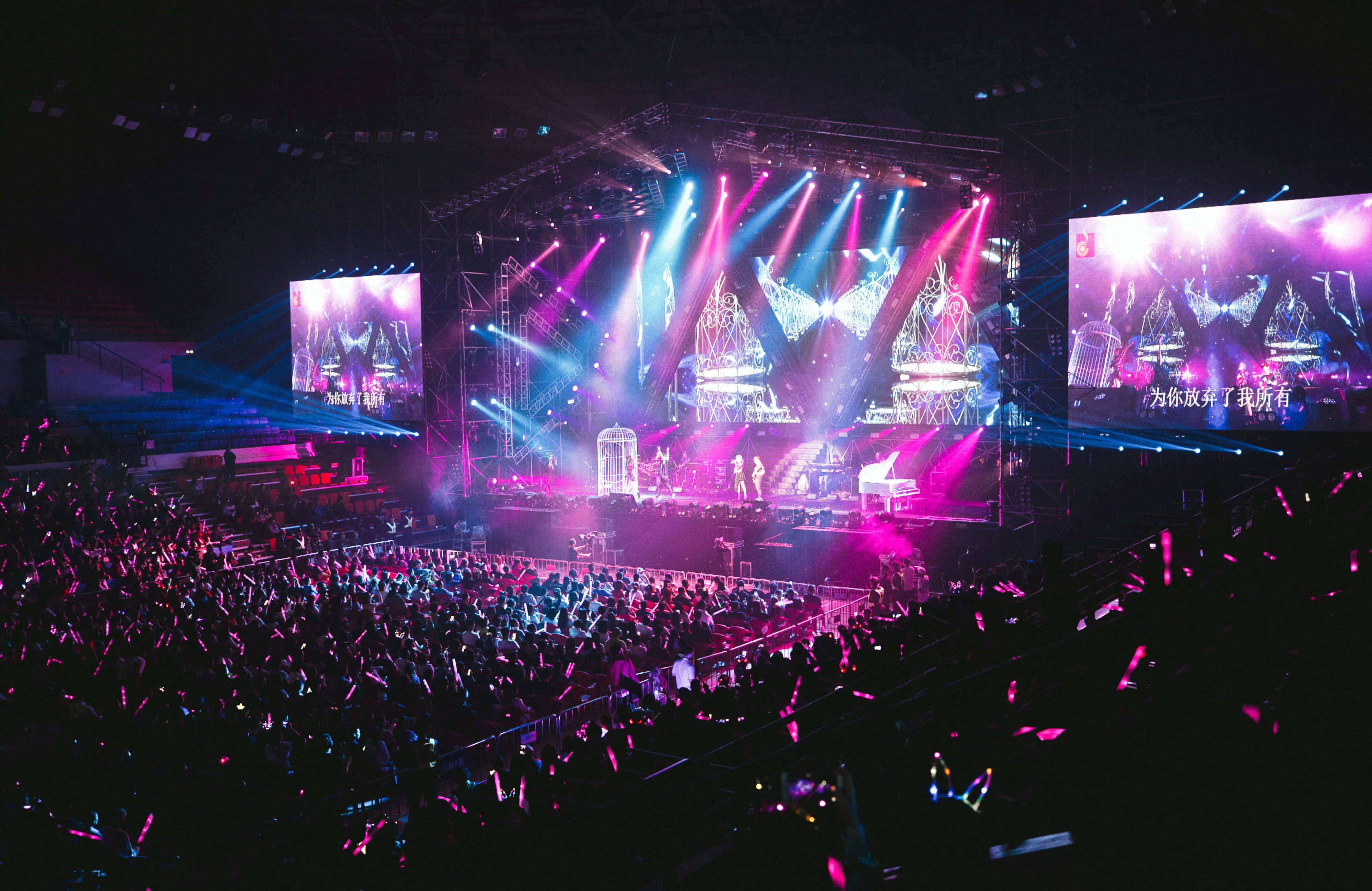 music festival 桌布 壁紙 — 一個充滿活力的音樂會舞台，沐浴在粉紅色和藍色的燈光中，人群在漆黑的夜空下揮舞著發光棒。