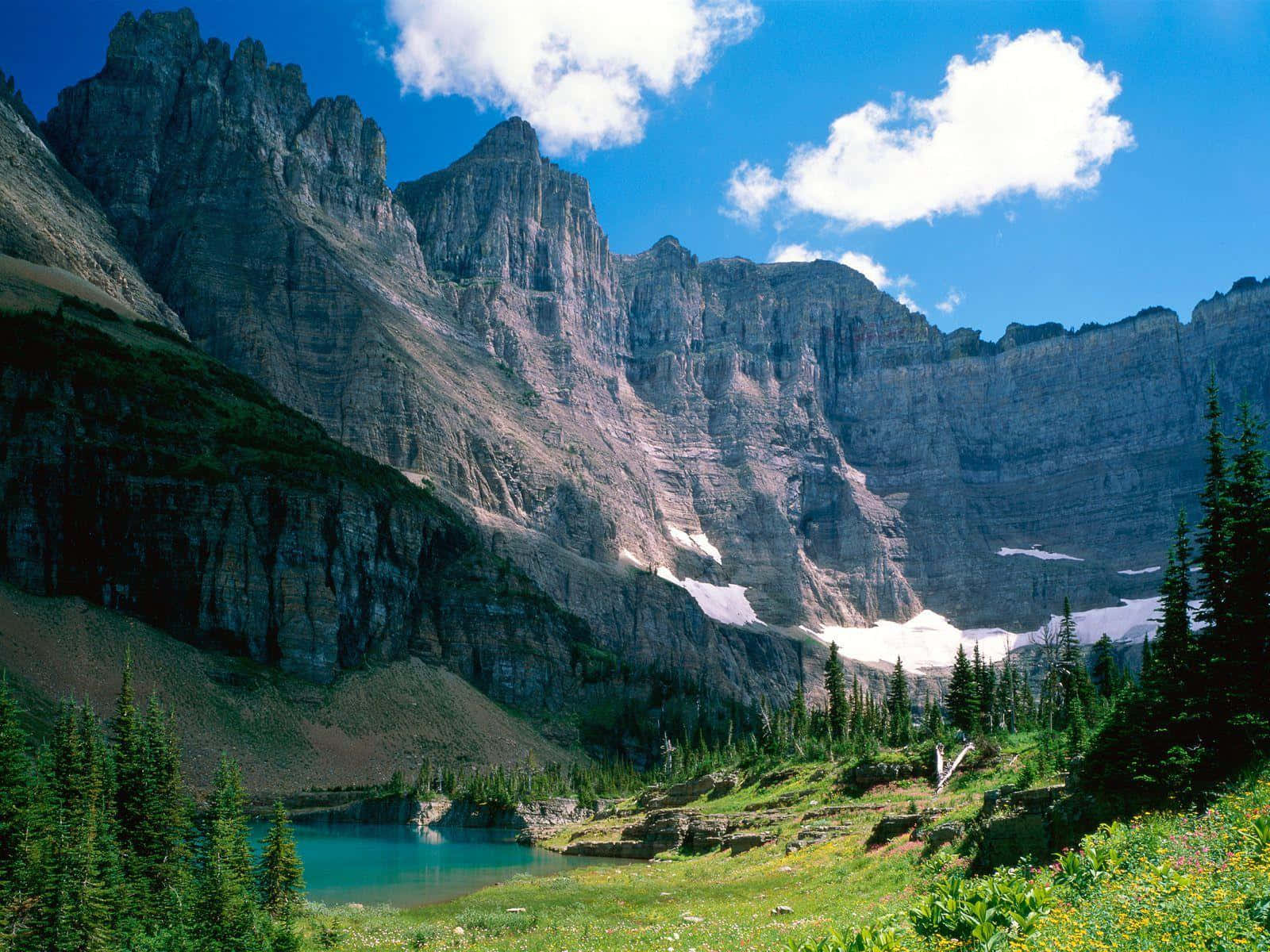 Montana 桌布 壁紙 — 一個充滿活力的高山湖泊映照著高聳的花崗岩懸崖，天空湛藍，點綴著蓬鬆的白雲。