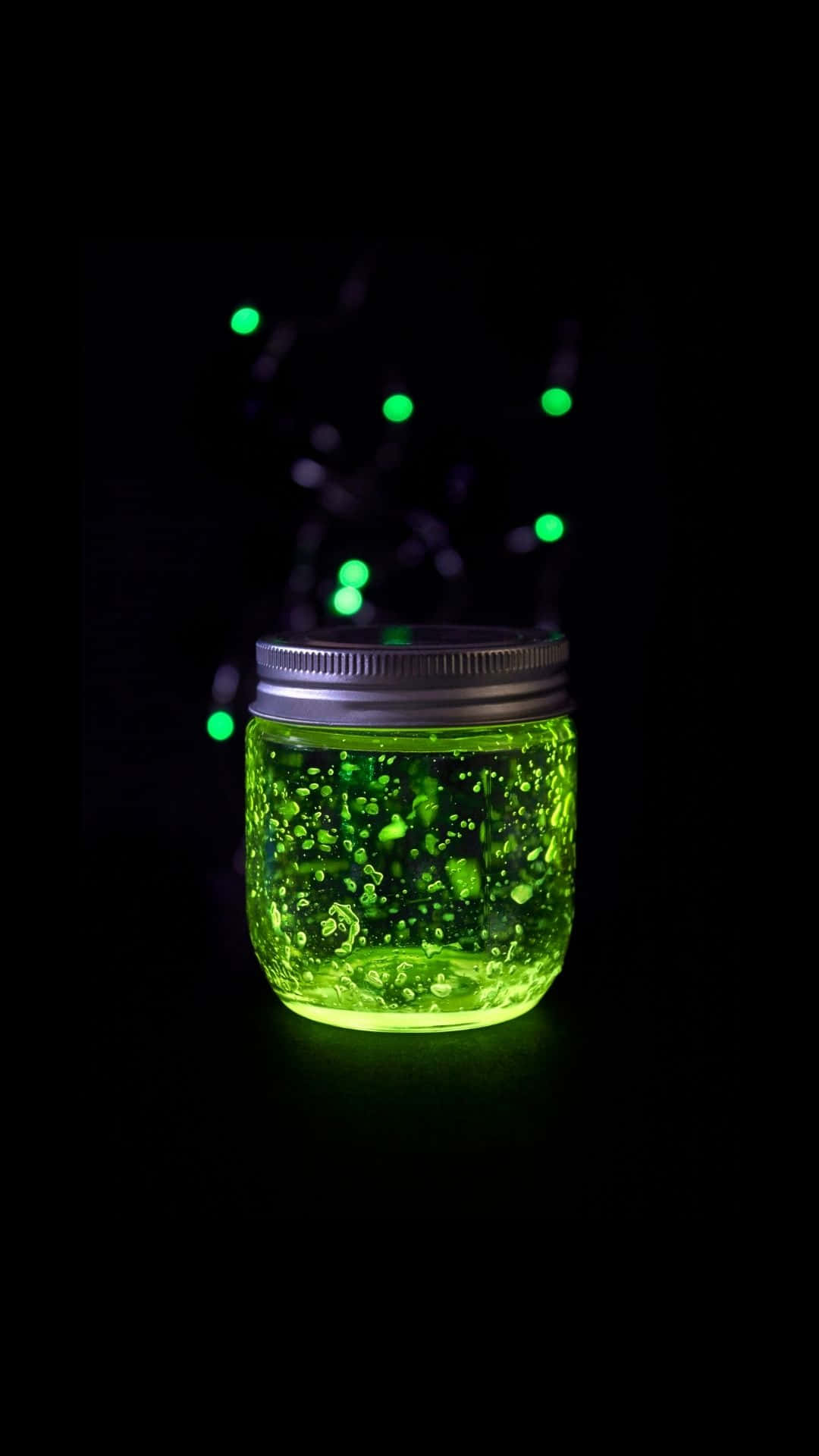 Glow In The Dark 桌布 壁紙 — 一個充滿發光綠色液體的梅森罐，帶有氣泡和串燈，背景黑暗。