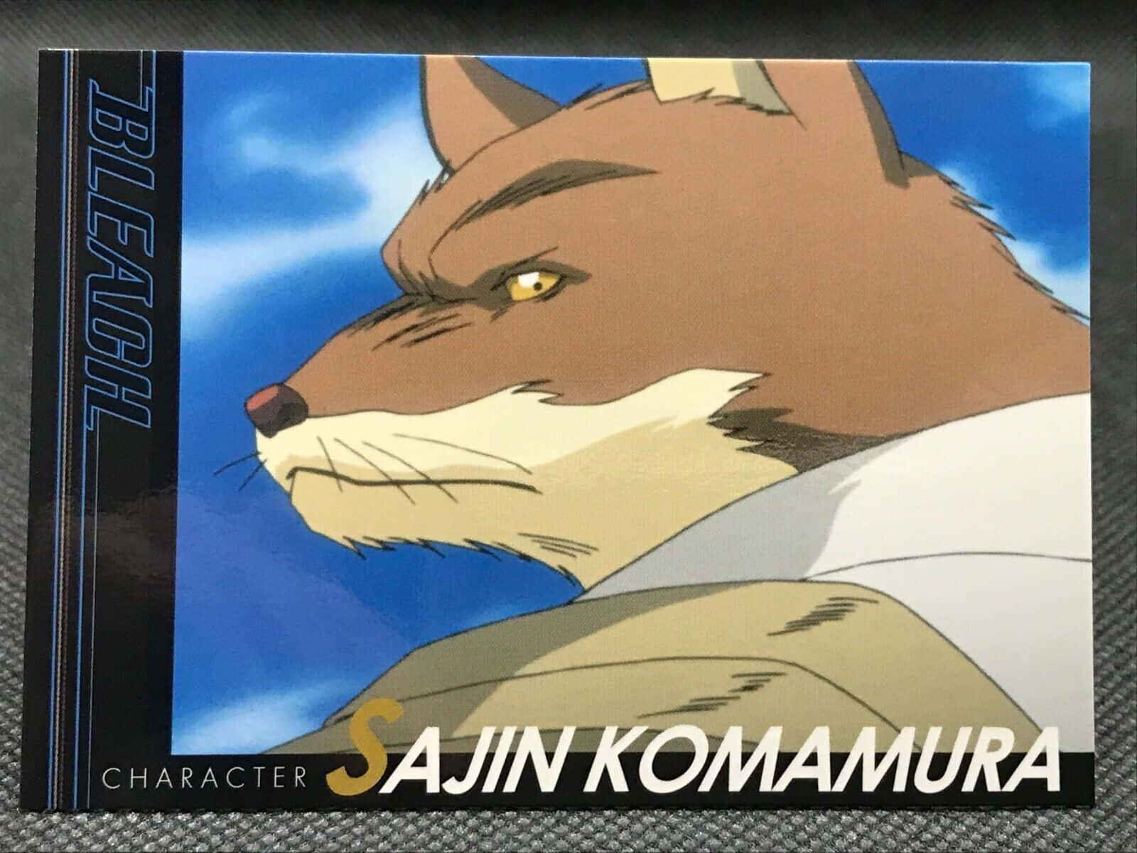 Sajin Komamura 桌布 壁紙 — 一個兇猛嘅動畫狐狸角色，金色眼睛同啡色毛髮，喺明亮嘅藍天下專注地凝視。
