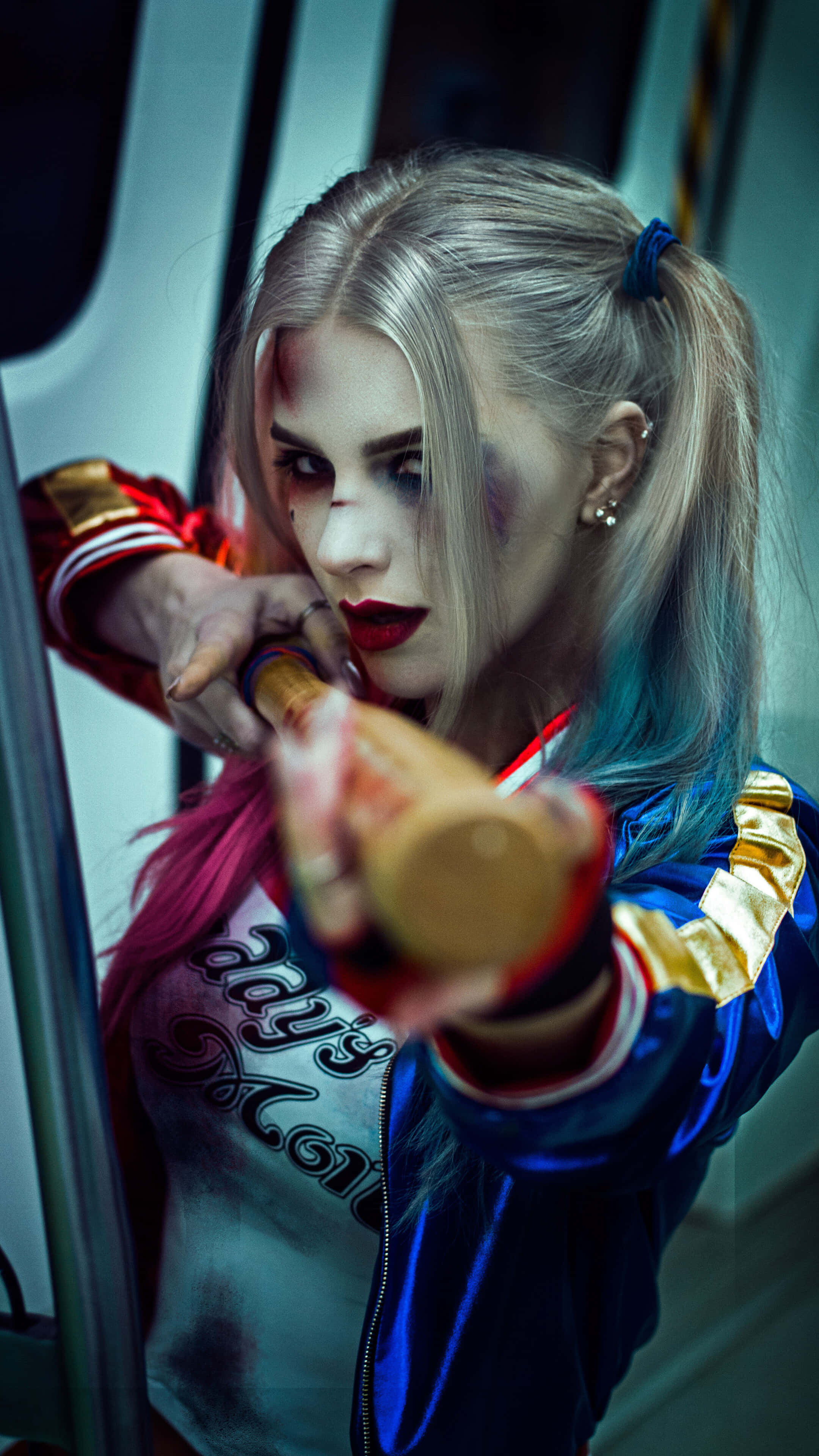 Harley Quinn Cosplay 桌布 壁紙 — 一個兇猛的哈莉·奎茵，身穿藍色外套和紅色手套，在昏暗的地鐵車廂內，專注地瞄準一支棒球棍。