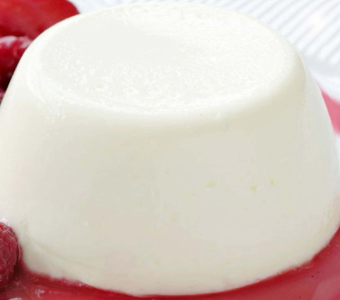 Blancmange 桌布 壁紙 — 一個光滑奶油般的白色意式奶凍圓頂，浸在鮮紅的覆盆子醬中，旁邊放有新鮮漿果。