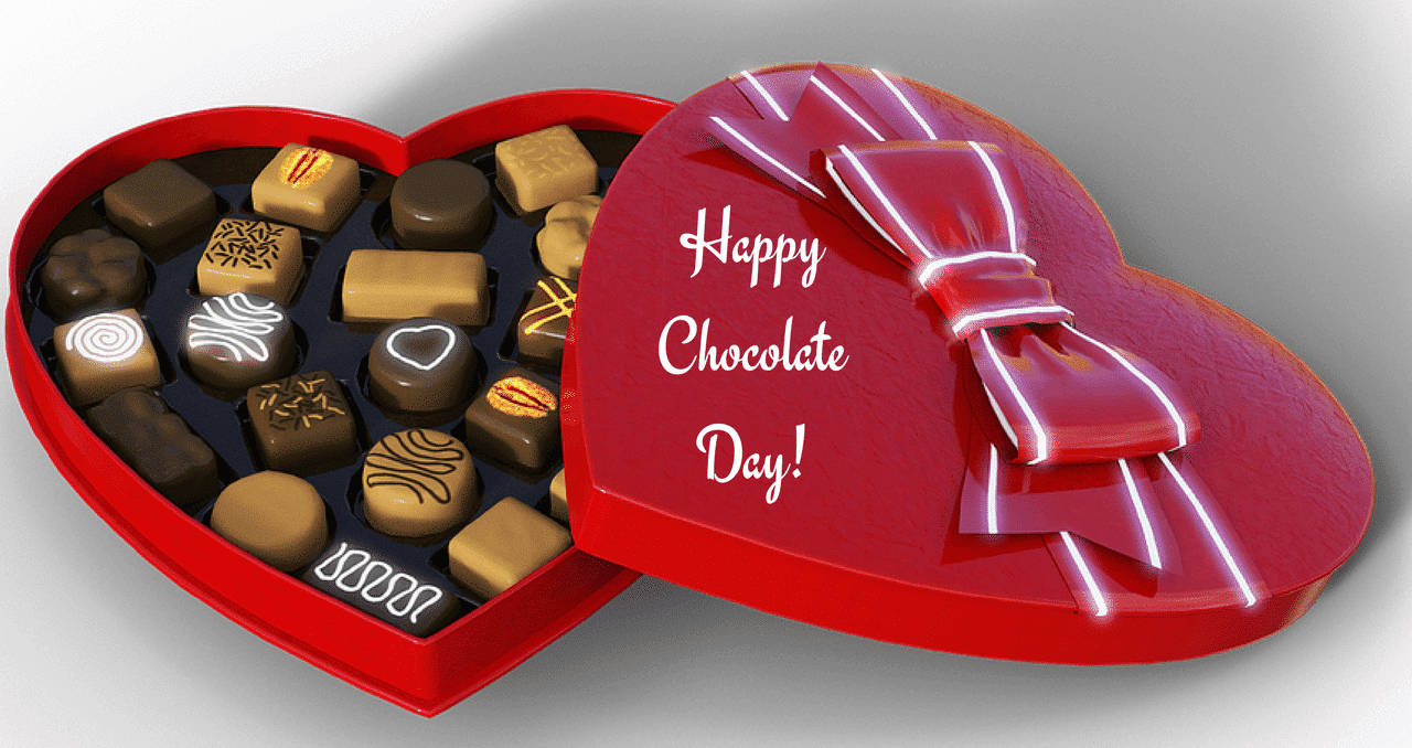 Chocolate Day 桌布 壁紙 — 一個光滑的紅色心形盒子，裝滿各種朱古力，頂部有蝴蝶結和Happy Chocolate Day訊息。
