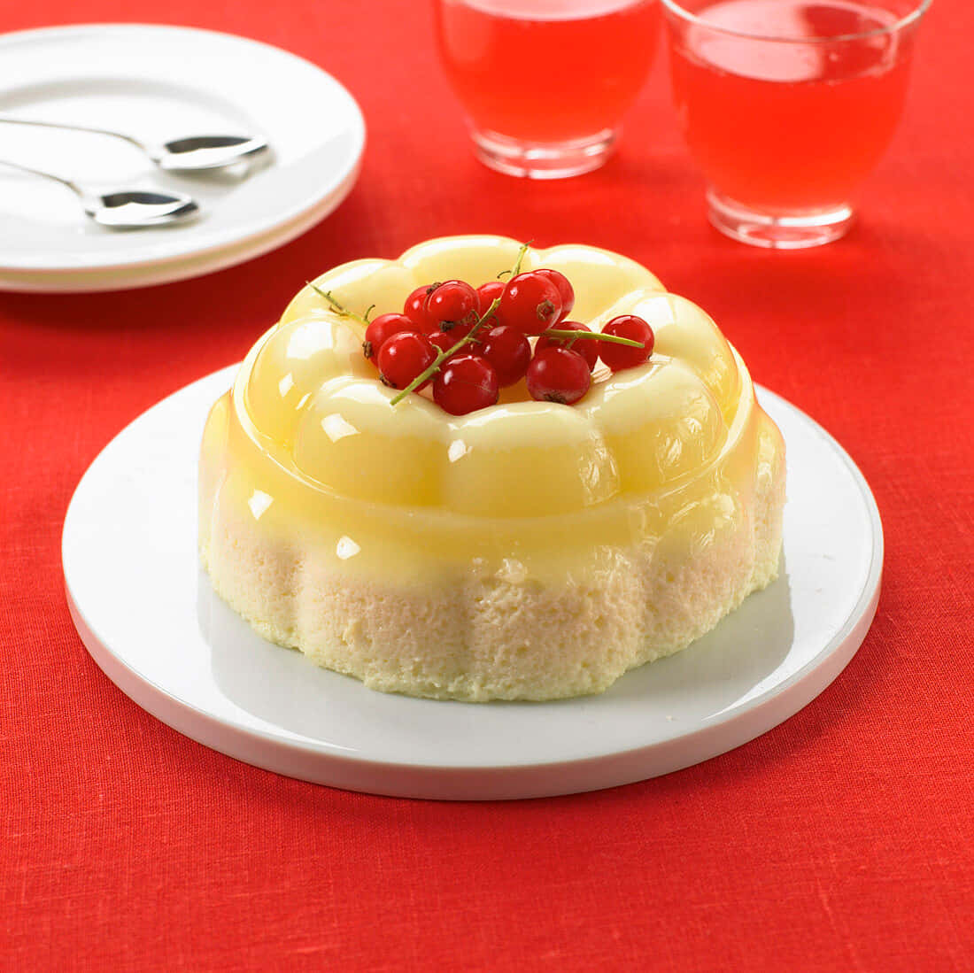 Blancmange 桌布 壁紙 — 一個光滑的黃色果凍甜品，上面放有紅加侖子，放在白色碟子上，襯以鮮紅色枱布。