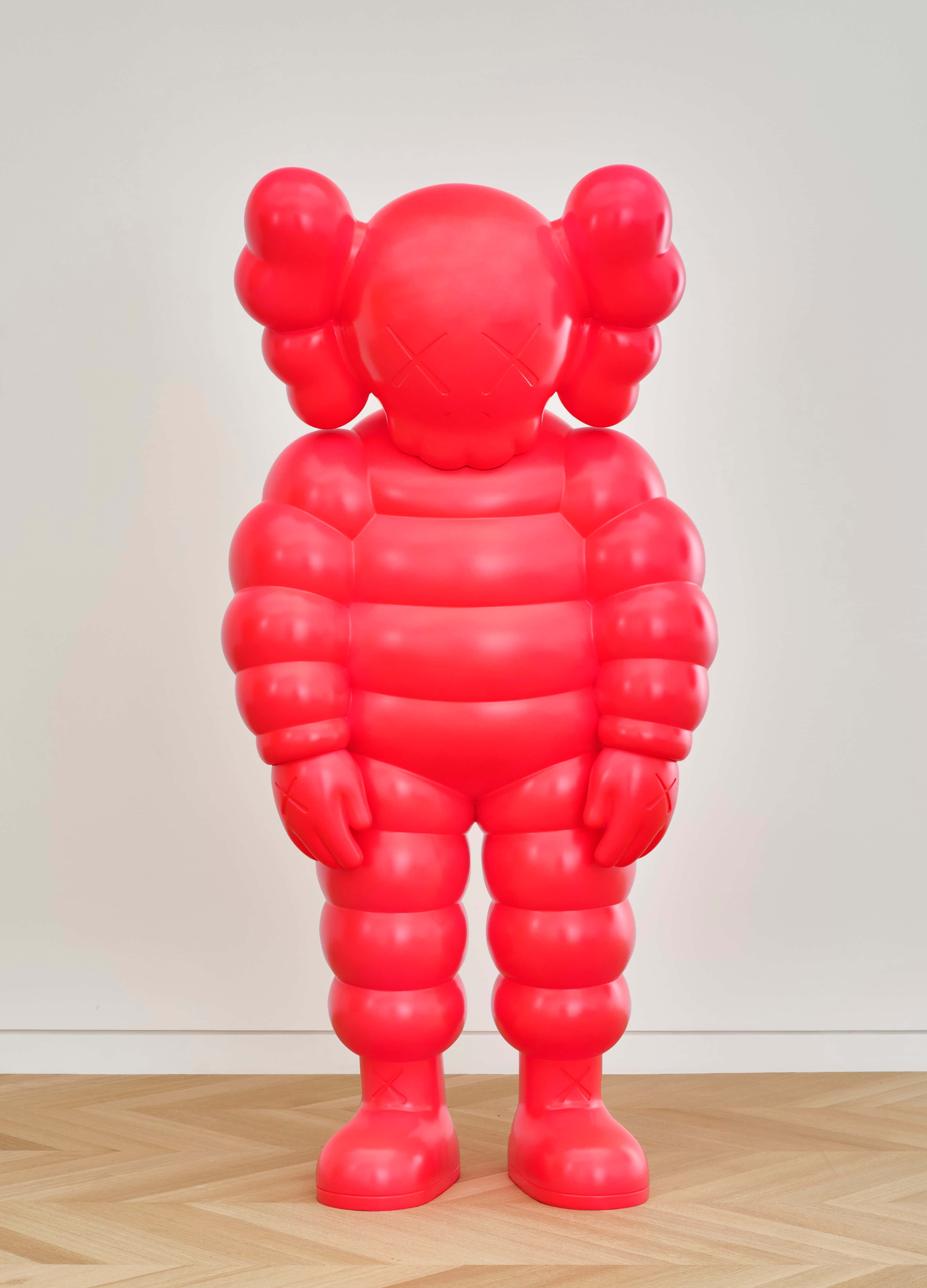 Kaws Chum 桌布 壁紙 — 一個光澤亮麗的紅色KAWS Companion雕塑高高地站在木地板上，背景是純白牆壁。