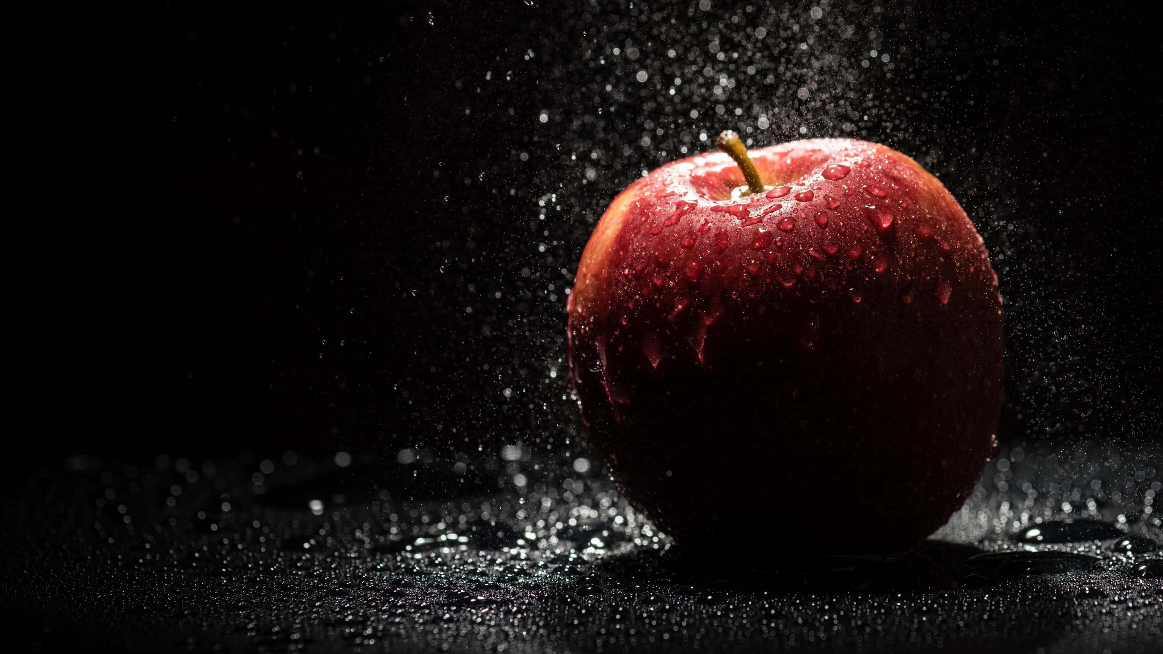 4K Apple 桌布 壁紙 — 一個光澤的紅蘋果在純黑背景上濺起水珠。