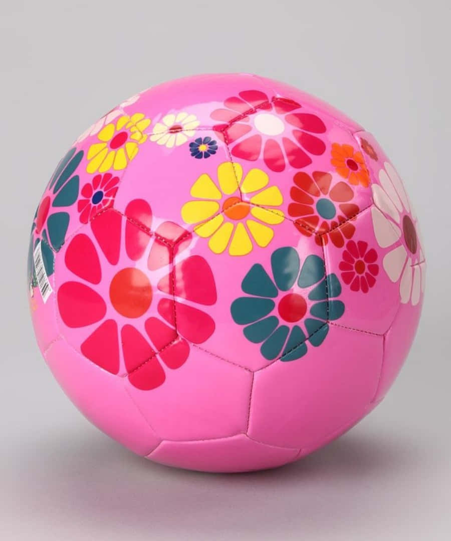 Pink Soccer Ball 桌布 壁紙 — 一個光澤粉紅色足球，飾有鮮豔的復古風格花朵，顏色有黃色、紅色和藍綠色，背景為中性灰色。