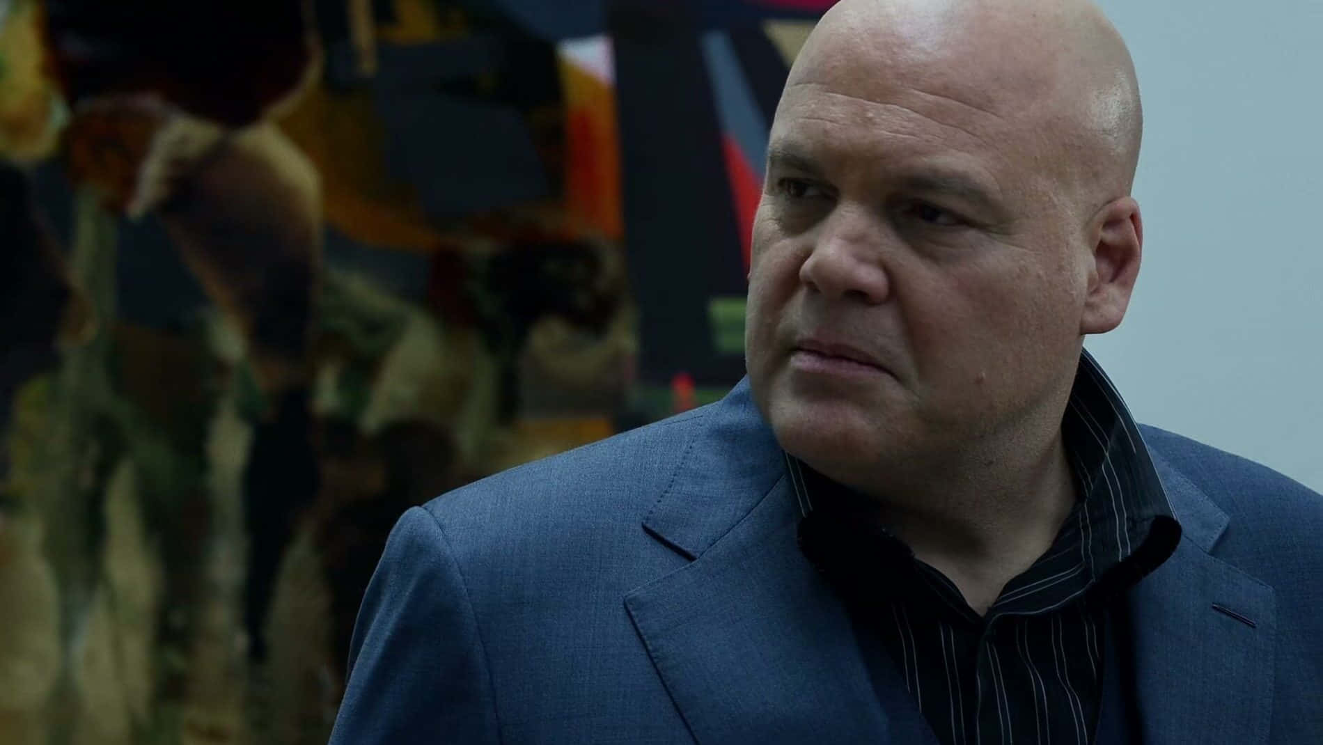 Vincent D'onofrio 桌布 壁紙 — 一個光頭男人穿著藍色西裝，在模糊多彩的背景前，表情嚴肅地望向鏡頭外。