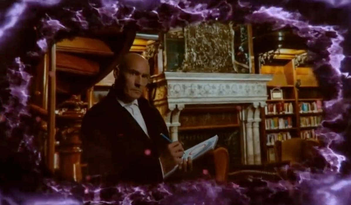 Grant Morrison 桌布 壁紙 — 一個光頭穿西裝的男人在一個由旋轉紫色能量框著的豪華圖書館內寫筆記本。