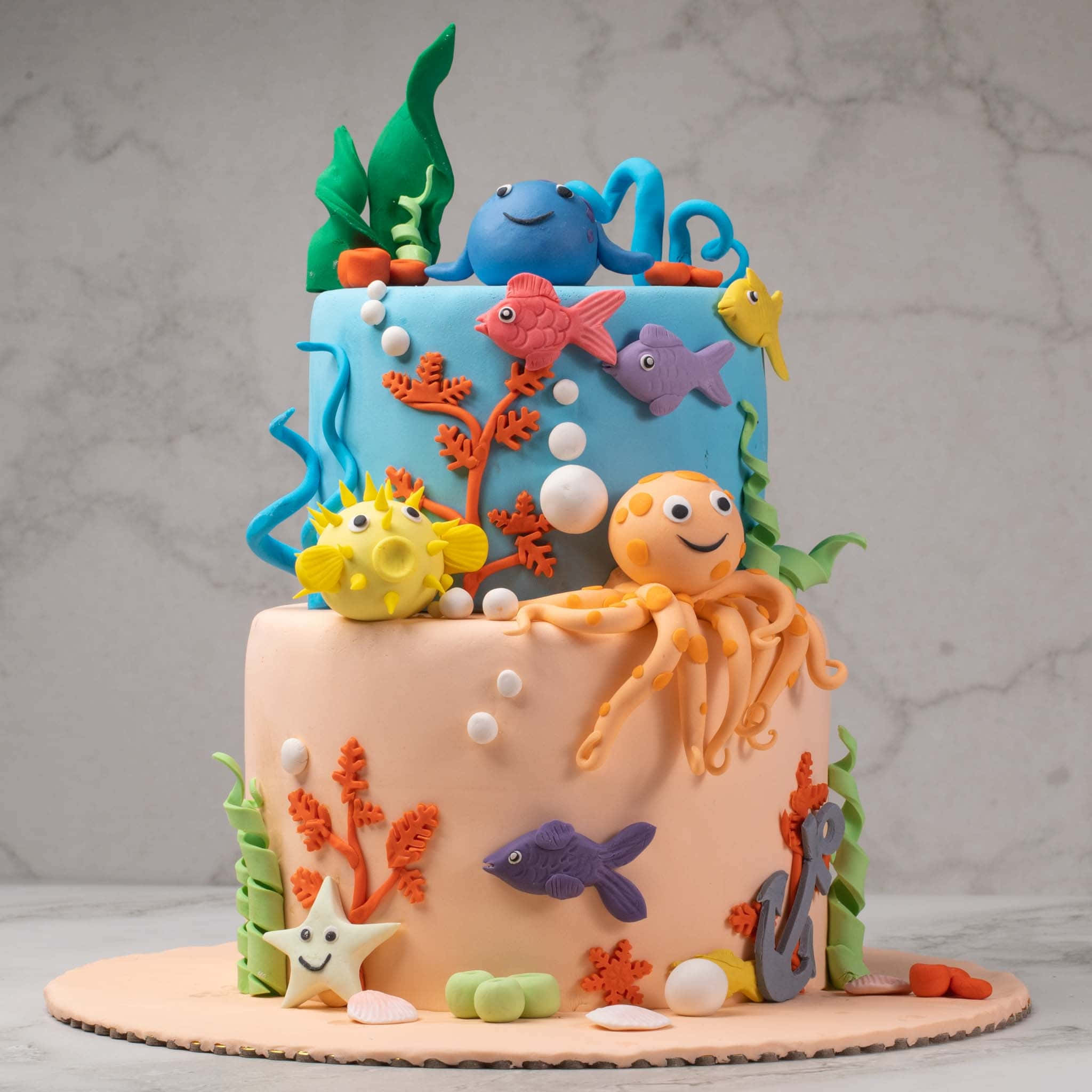 Cake Fondant 桌布 壁紙 — 一個兩層蛋糕，裝飾有彩色翻糖海洋生物、珊瑚和氣泡，背景為大理石紋。