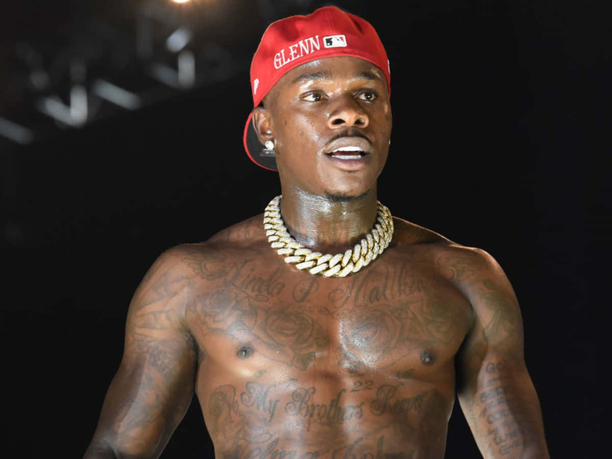 Dababy 桌布 壁紙 — 一個冇著衫嘅男人，身上有紋身，戴住紅色帽同粗金鏈，背景係深色。