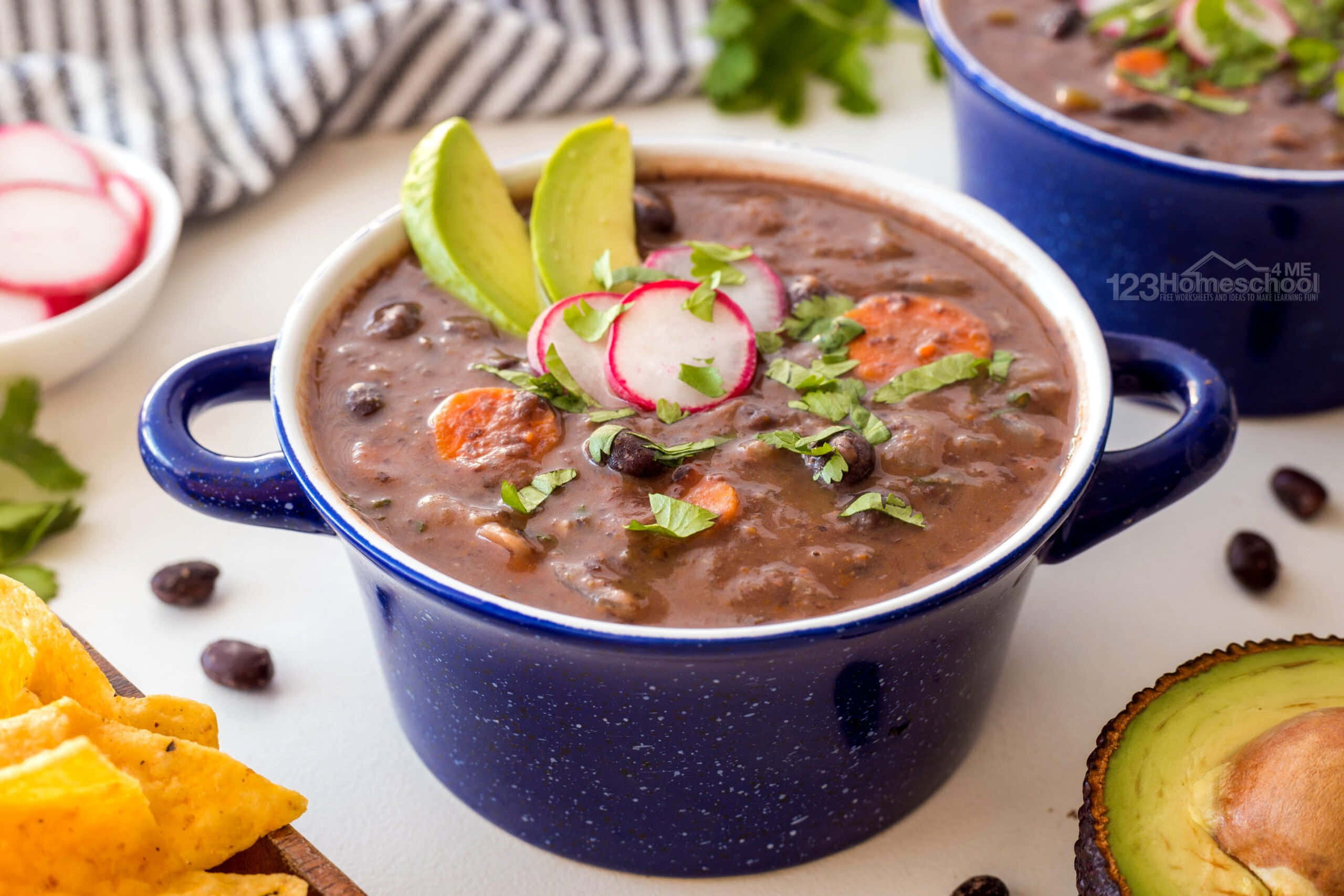 Black Bean Soup 桌布 壁紙 — 一個冒著蒸氣的藍色琺瑯碗，盛滿濃郁的黑豆湯，上面放著牛油果片、蘿蔔片和新鮮芫荽。