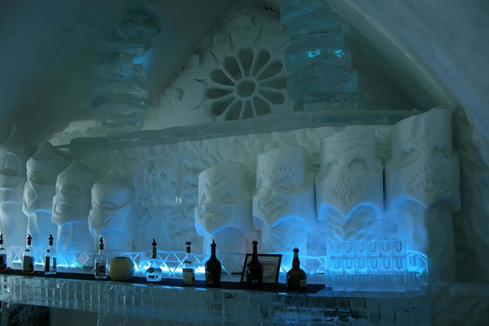 Ice Hotel 桌布 壁紙 — 一個冰吧，在冰冷的櫃檯上，瓶子下方有雕刻的提基面具和發光的藍色燈光。