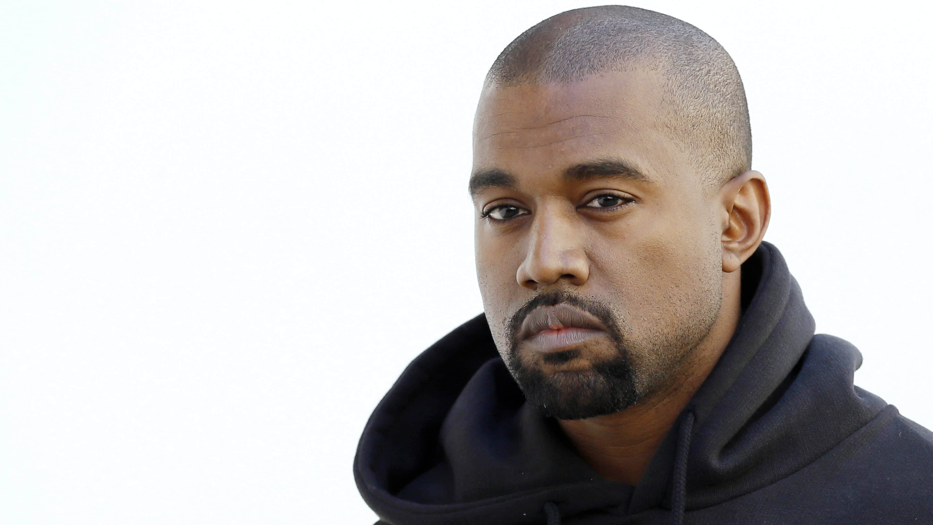 Kanye West Clean Black Hoodie 壁紙 — 一個剃光頭、留山羊鬍的男人穿著黑色連帽衫，在純白背景前的特寫肖像。