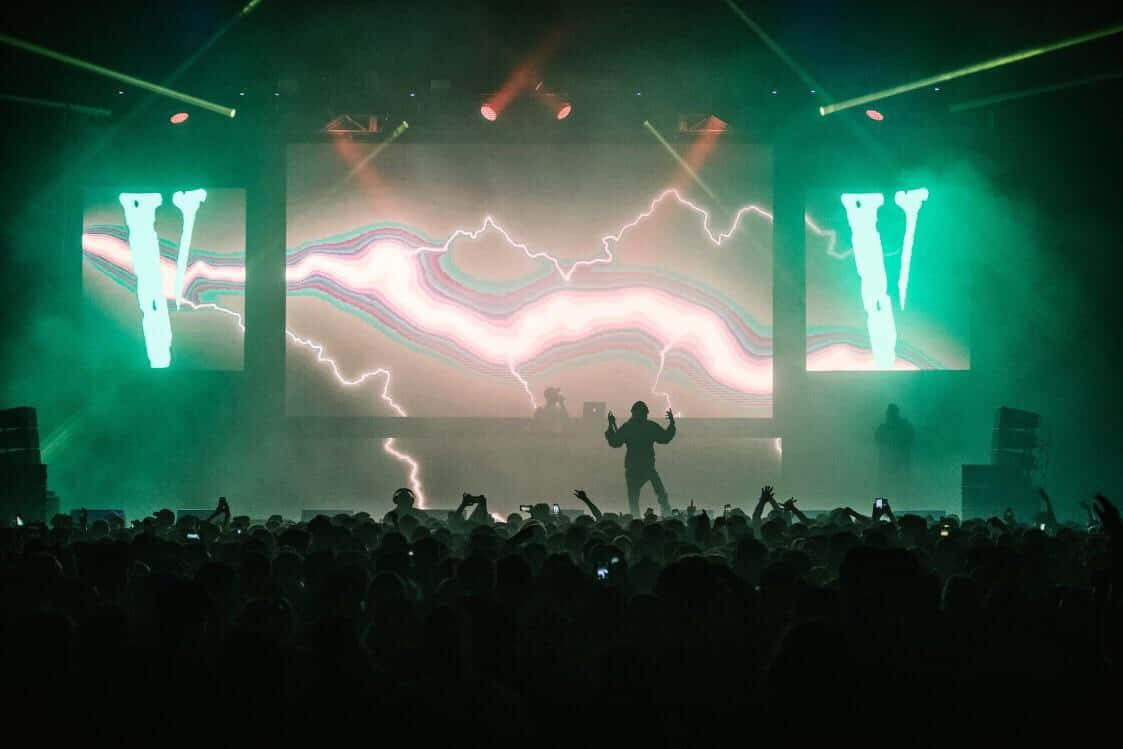 DJ在熱鬧的夜間音樂會上表演，身後有發光的閃電視覺效果。 — Playboi carti GIF 壁紙
