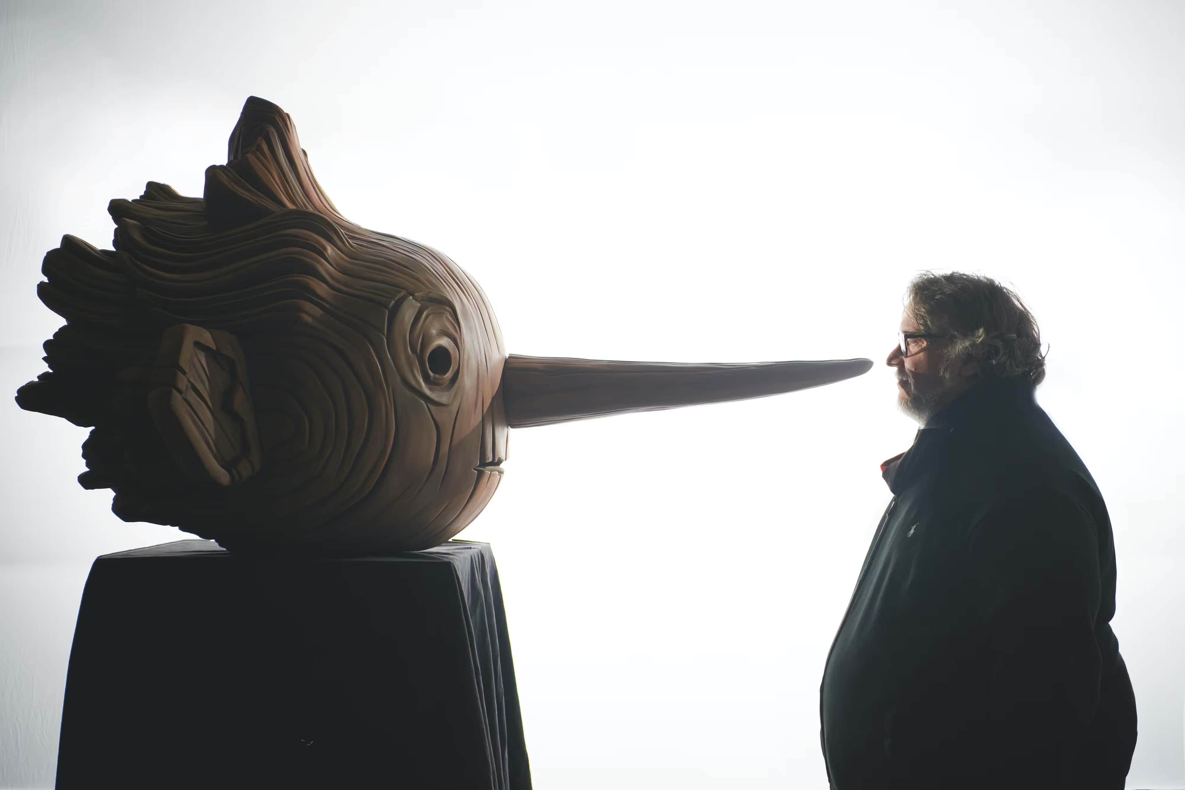 Guillermo Del Toro's Pinocchio 桌布 壁紙 — 一個剪影中的男人凝視著一個大型木製鳥類雕塑，鳥有長喙，背景是明亮的白色。