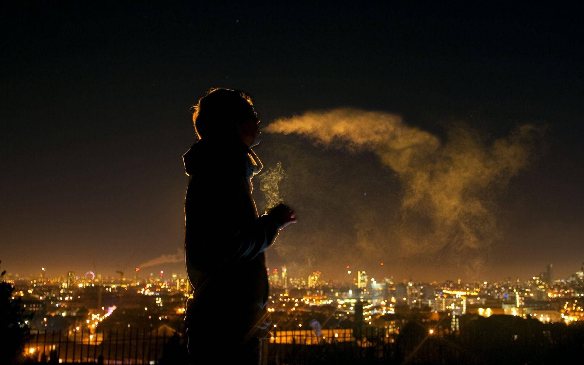 Silhouette 桌布 壁紙 — 一個剪影人物在充滿活力的夜間城市景觀中呼出一團發光的煙霧。