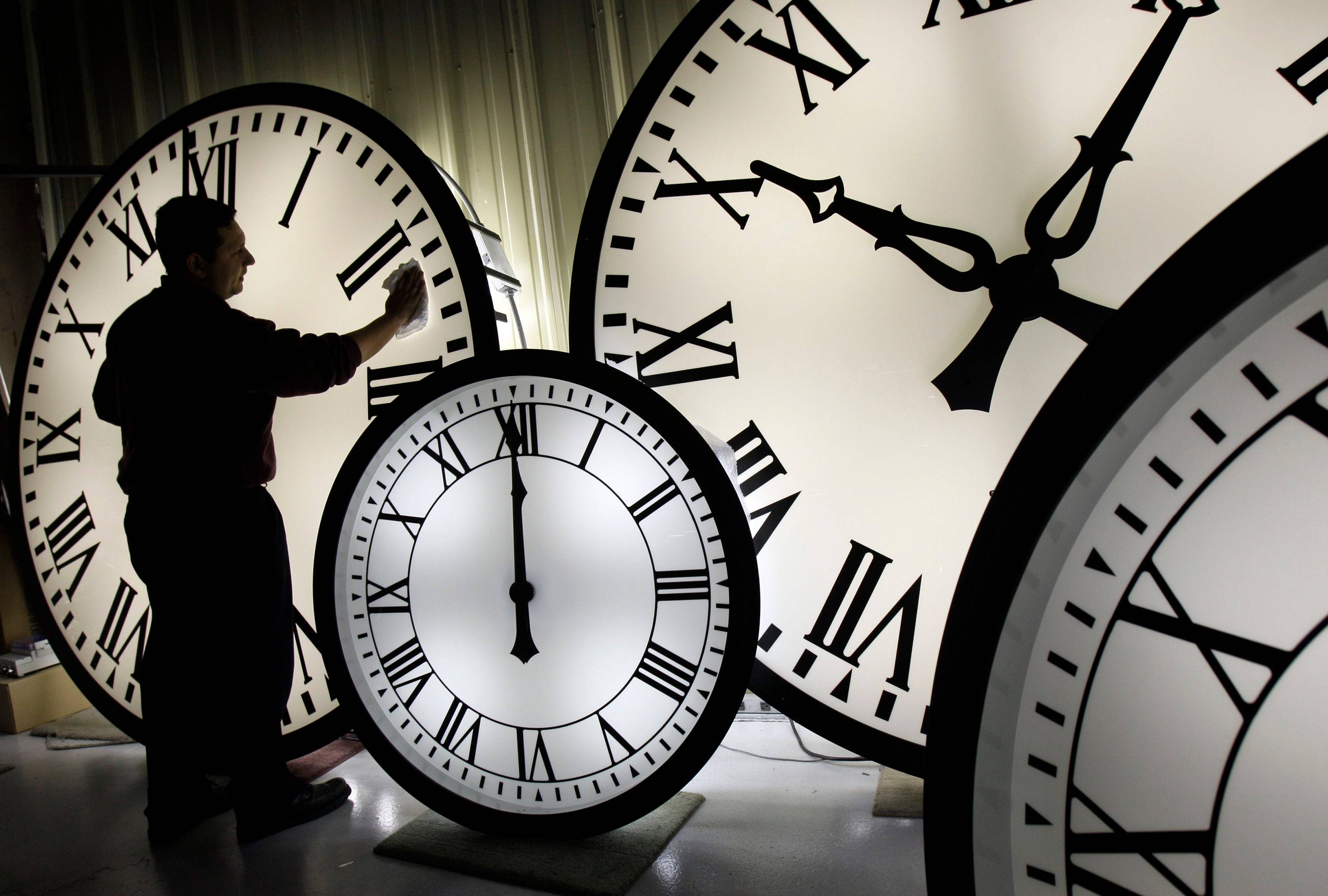 Clock 桌布 壁紙 — 一個剪影工人喺昏暗嘅工場入面，喺幾個巨大嘅發光時鐘面之中，打磨其中一個。