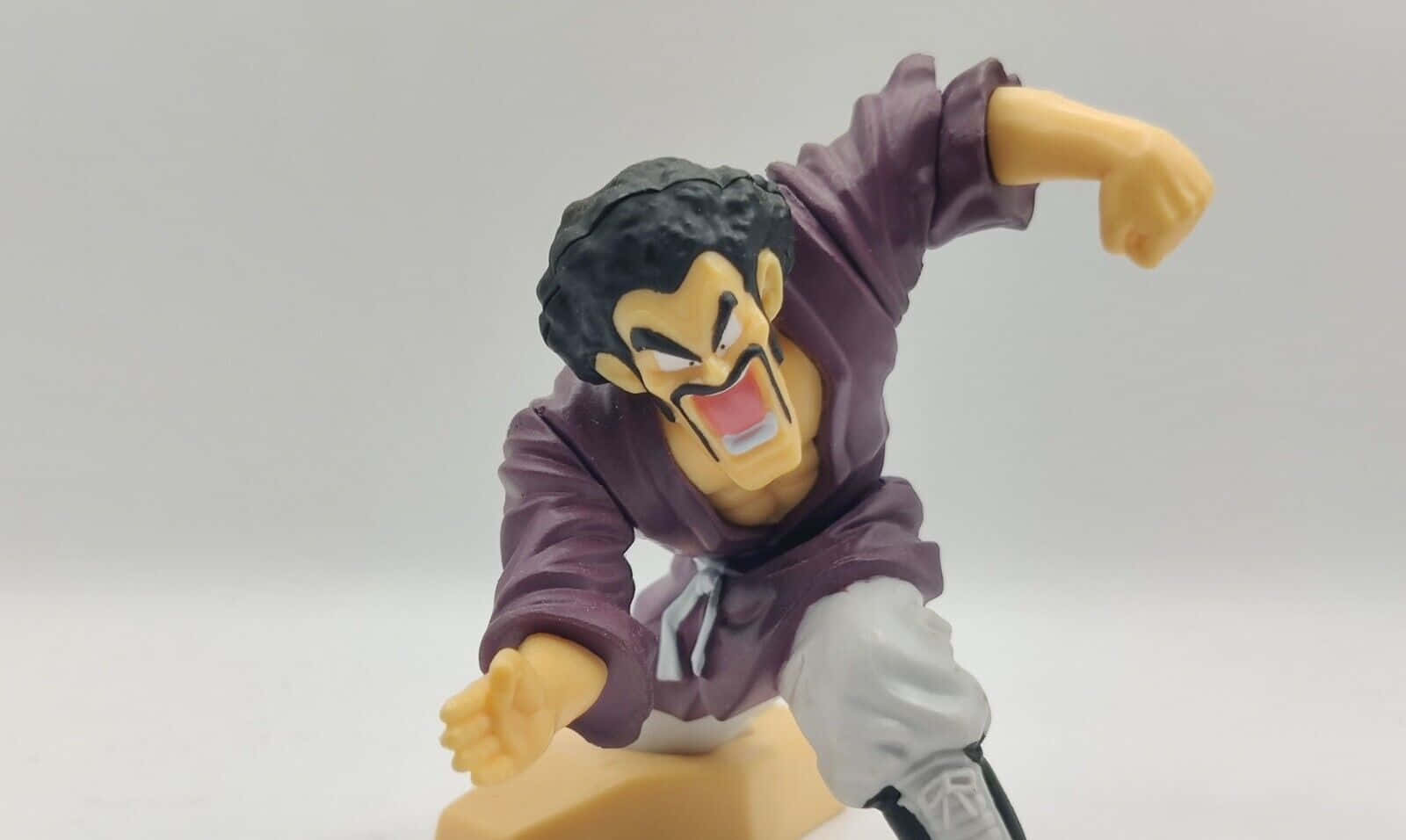 Hercule Satan 桌布 壁紙 — 一個動態動漫動作人偶，描繪一位肌肉發達的戰士穿著紫色道服，正以兇猛表情揮拳。