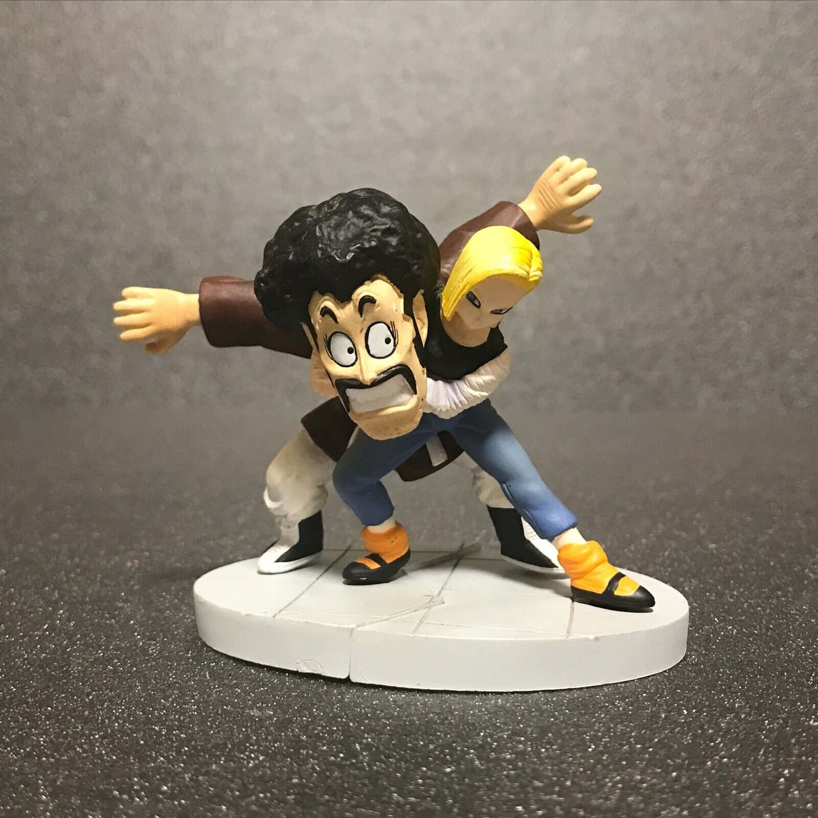 Hercule Satan 桌布 壁紙 — 一個動態動漫動作人偶描繪了一個肌肉發達、黑髮留鬚的男人與一個金髮女人在緊張的戰鬥姿勢中搏鬥。