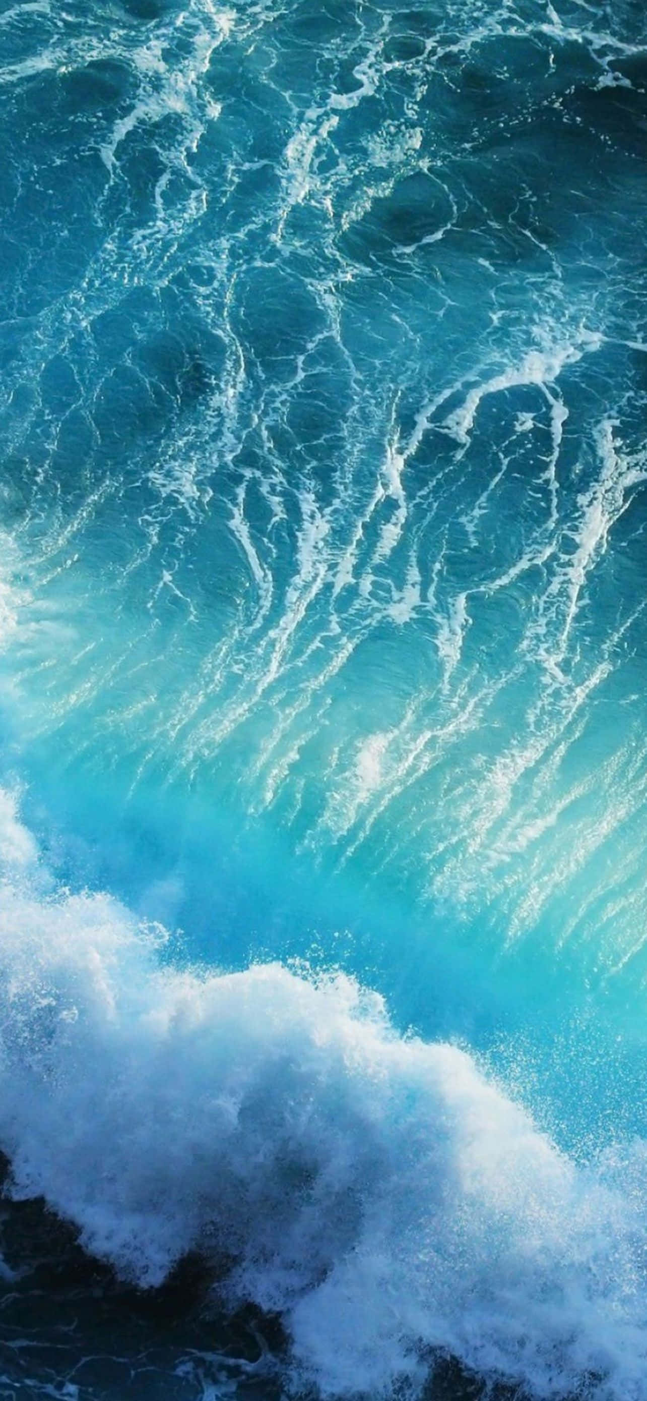 藍色 iPhone 桌布 壁紙 — 一個動態的特寫，呈現藍綠色海浪拍打著深藍色大海，激起白色泡沫。
