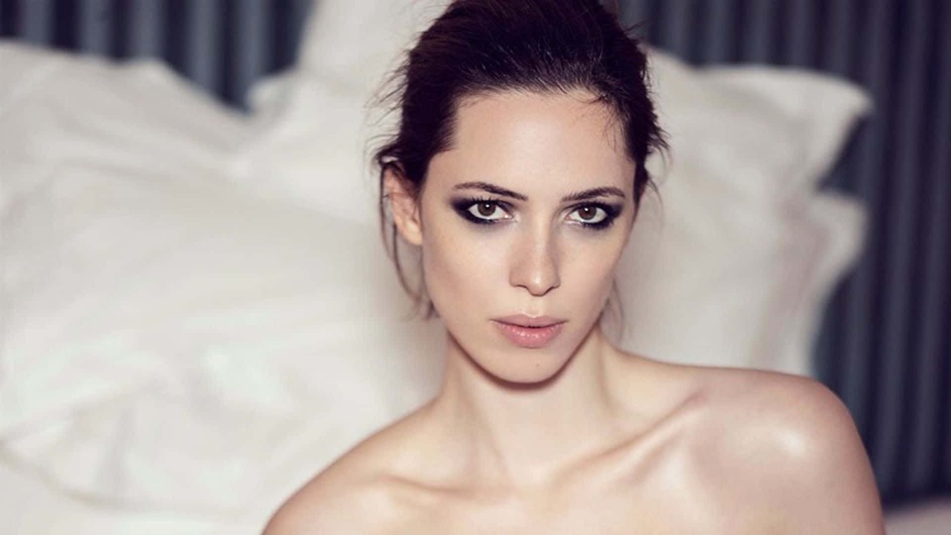 Rebecca Hall 桌布 壁紙 — 一個化著煙燻眼妝的女人，從一張鋪著皺巴巴白色床單的床上，投來強烈的目光。
