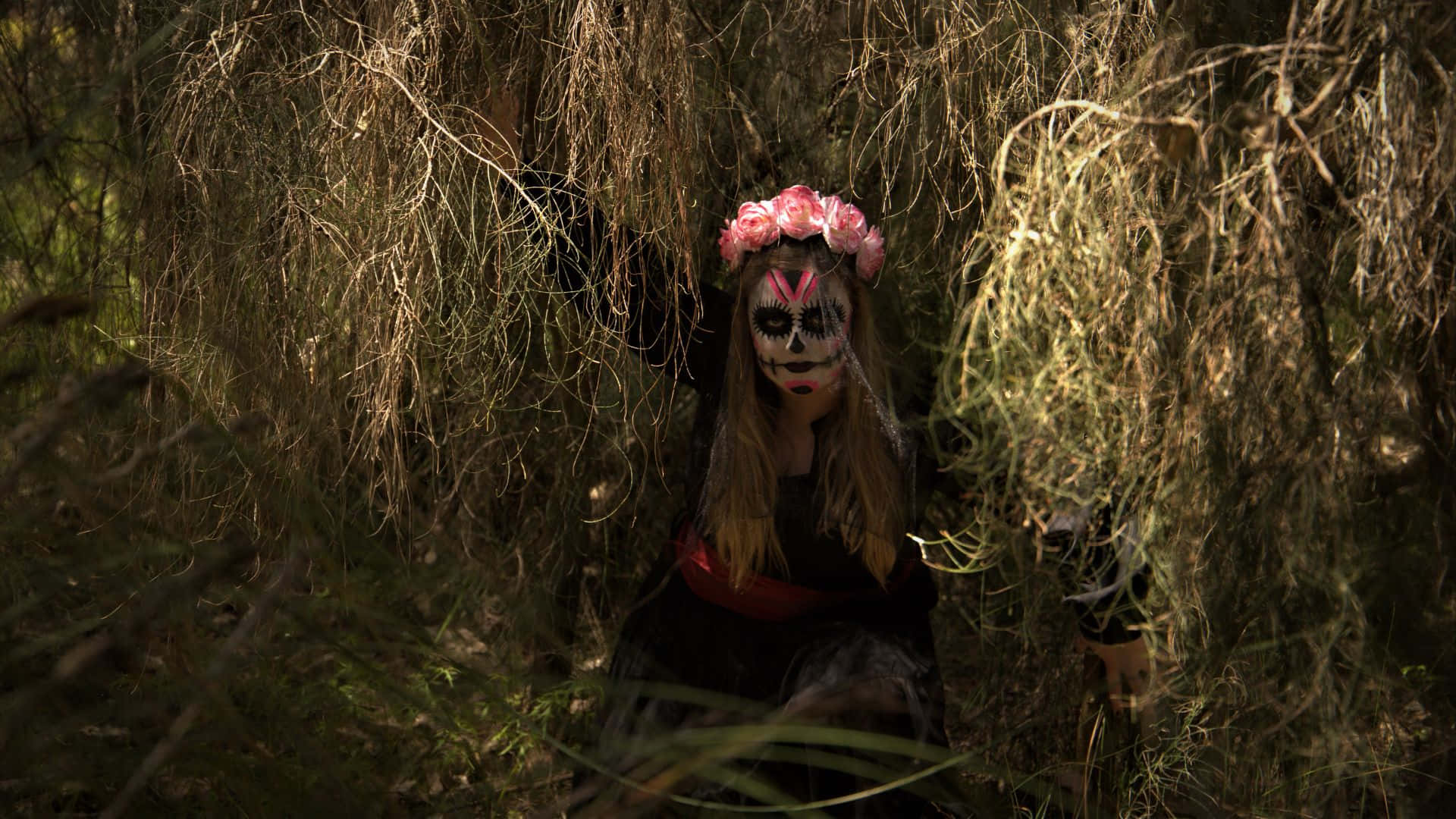 Horror Costumes 桌布 壁紙 — 一個化著骷髏妝、戴著粉紅色花冠的人，從陰暗森林中纏繞的乾枯藤蔓間探出頭來。