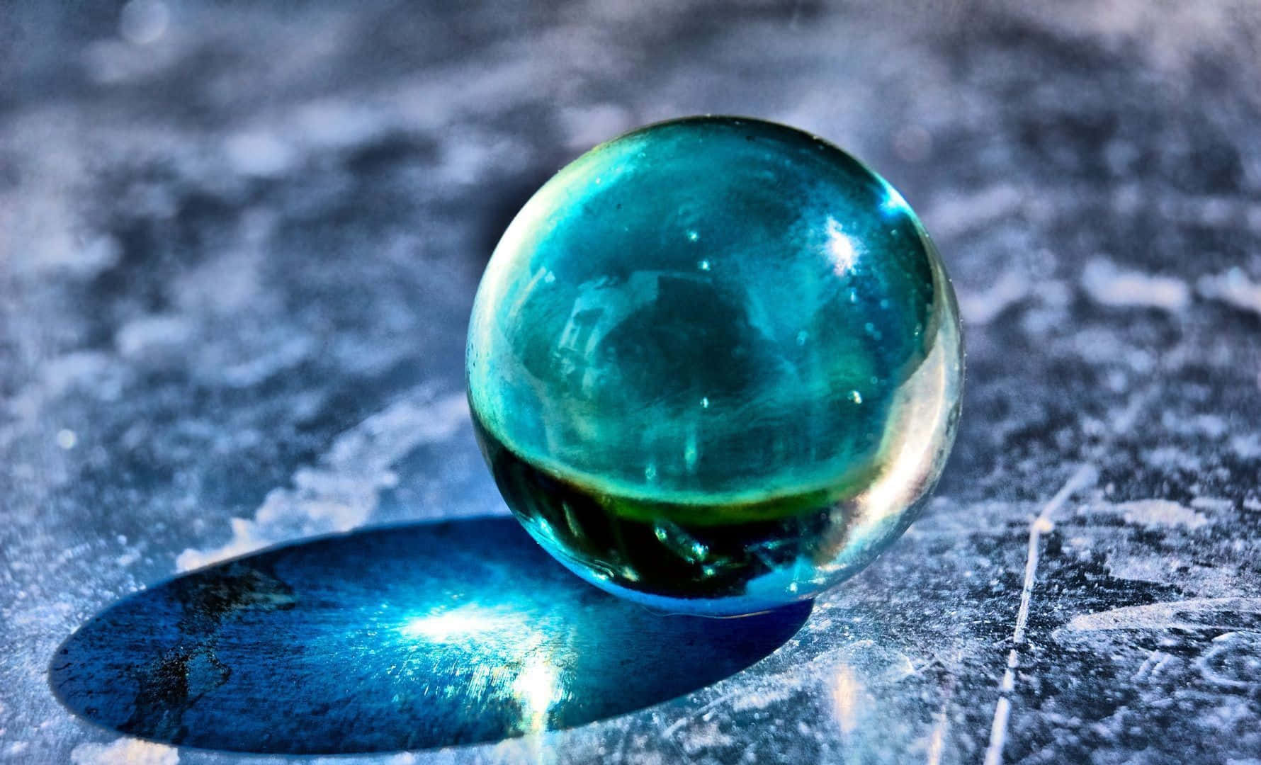 Crystal Ball 桌布 壁紙 — 一個半透明的青綠色玻璃球放置在帶有紋理的灰色表面上，投射出鮮豔的藍色陰影。