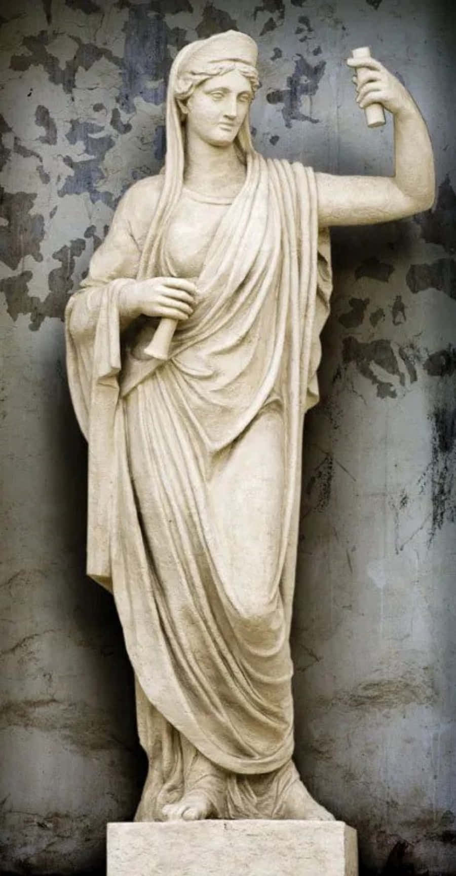 greek 桌布 壁紙 — 一個古典大理石雕像，描繪一位披著布料、手持卷軸的女性形象，立於風化質感的牆前。