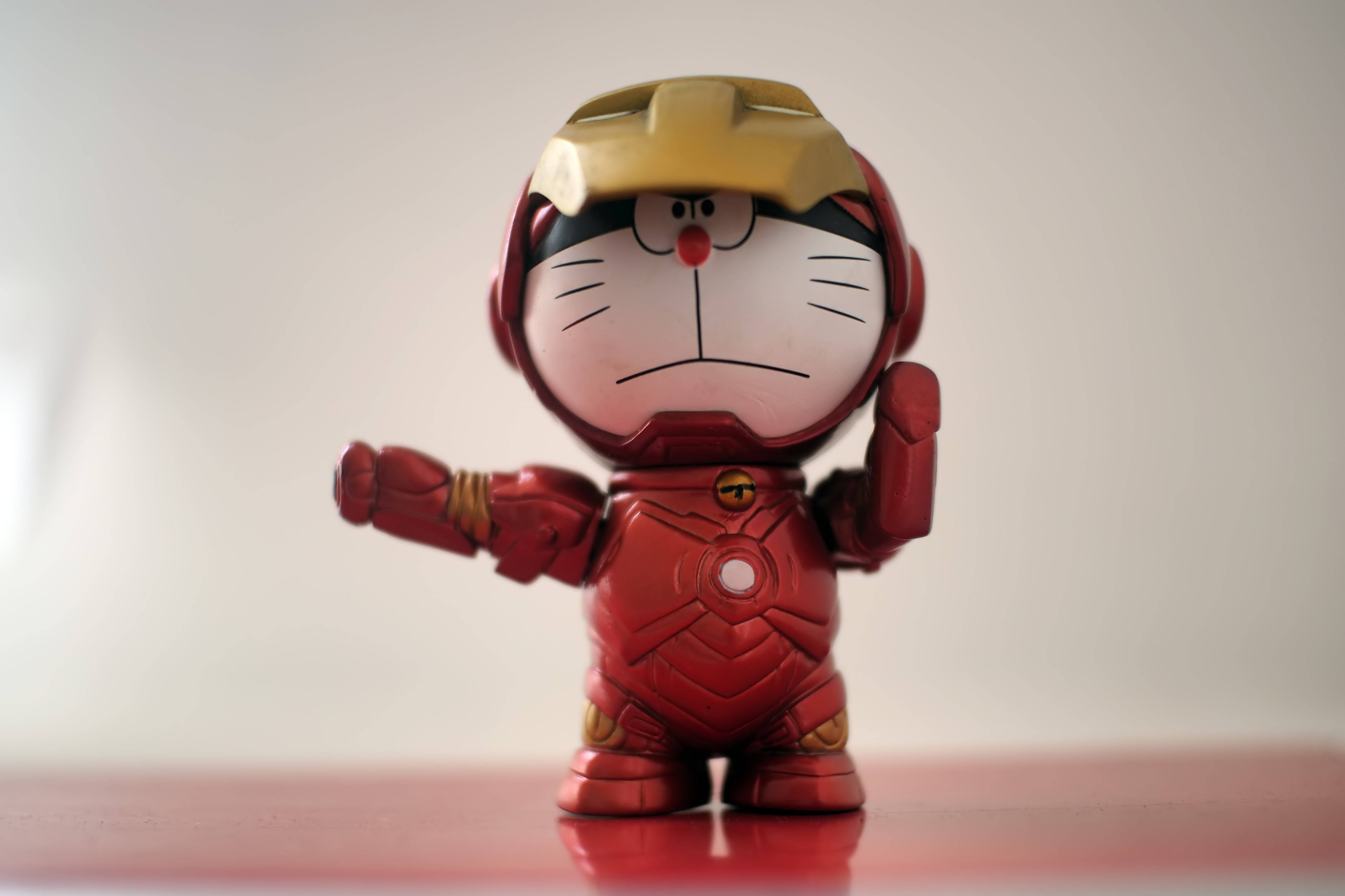 Doraemon 桌布 壁紙 — 一個可愛的哆啦A夢公仔穿著精細的紅色和金色鐵甲奇俠套裝，自信地站在反光表面上。