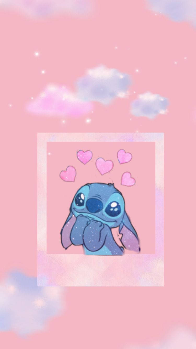 cute stitch iPhone 桌布 壁紙 — 一個可愛的藍色外星人，有大眼睛和漂浮的粉紅色心形，背景是柔和的粉紅色天空和蓬鬆的雲朵。